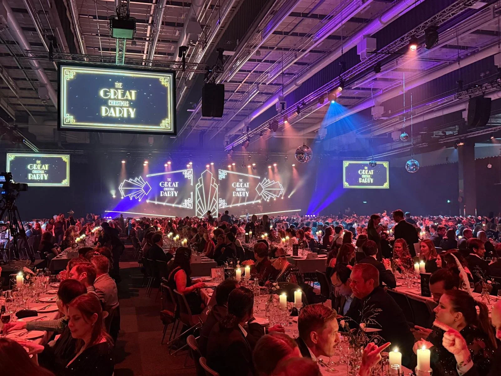 En stor inomhusscen med band och ljusdesign för en julfest, många gäster sitter vid dukade bord.