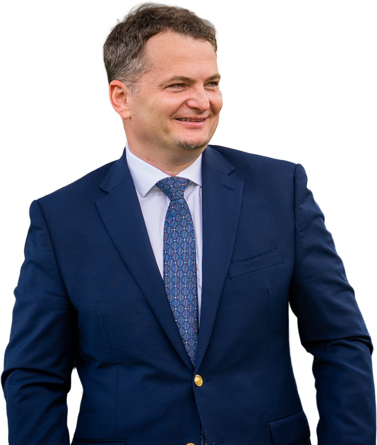 Eugen, who has short brown hair wearing a navy blue suit, light blue shirt, and patterned tie, smiling and standing outdoors.
