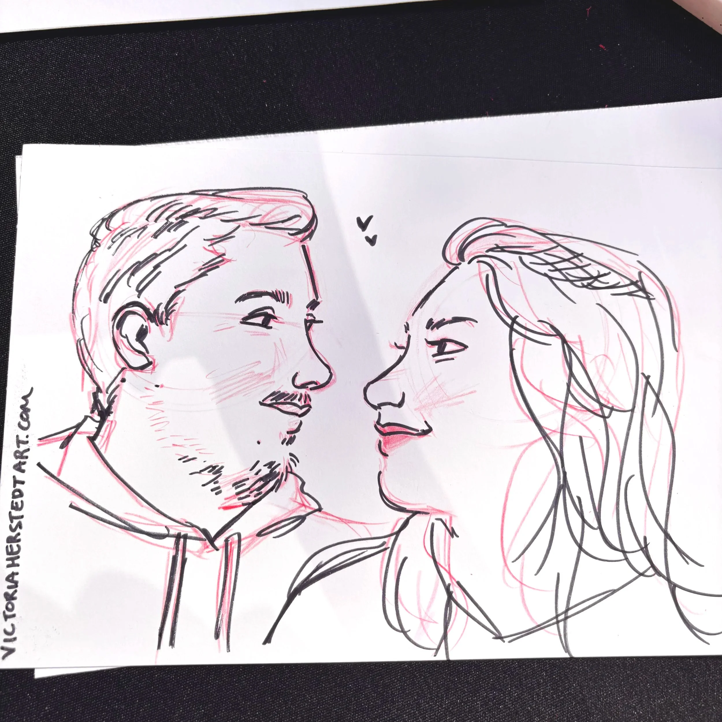 A drawing of a couple (man and a woman) in ink pen and red colored pencil done at an alternative wedding expo at the Victorian Belle.