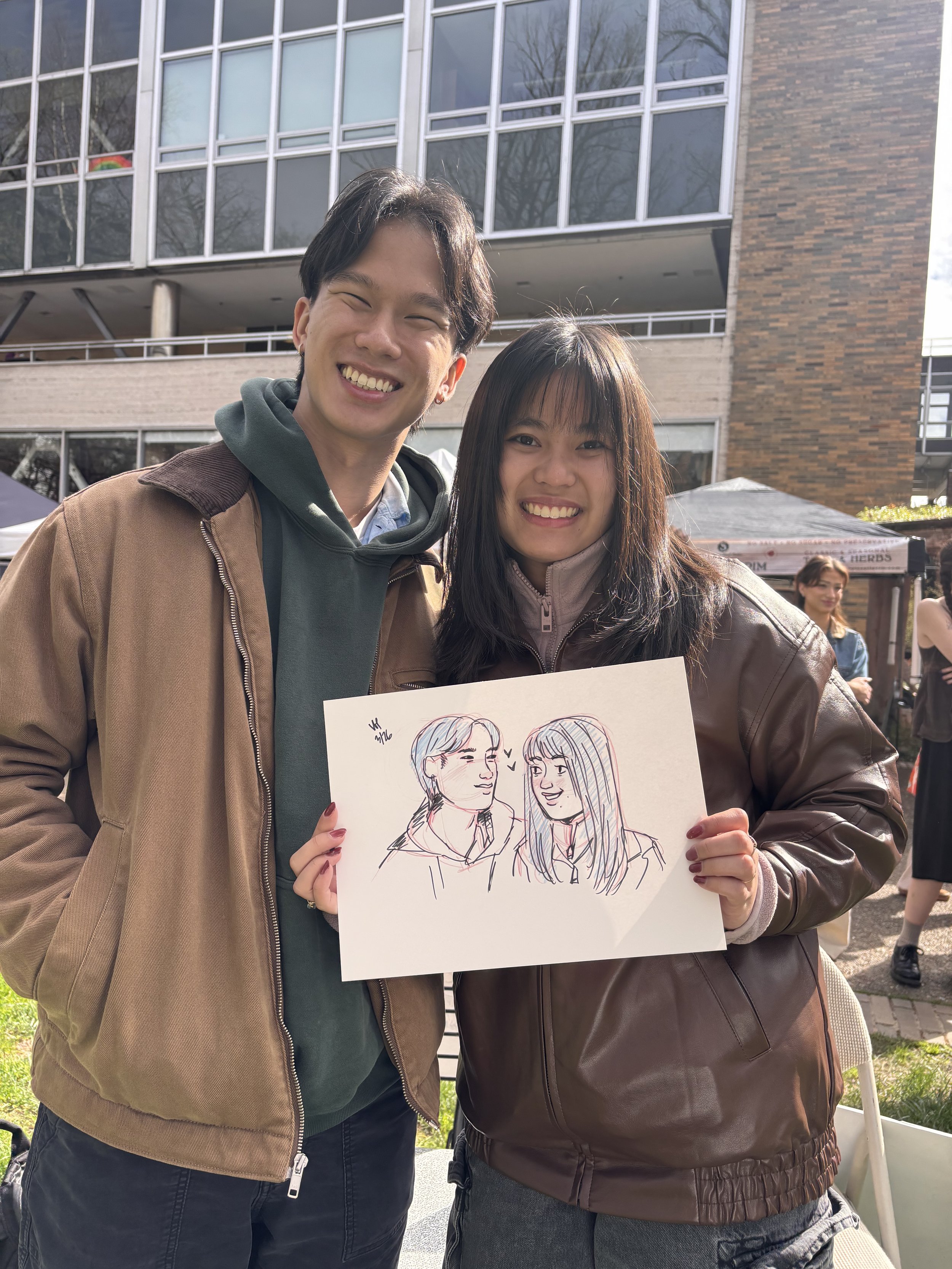 Young couple holding their live portrait drawing at the PSU Farmers Market.