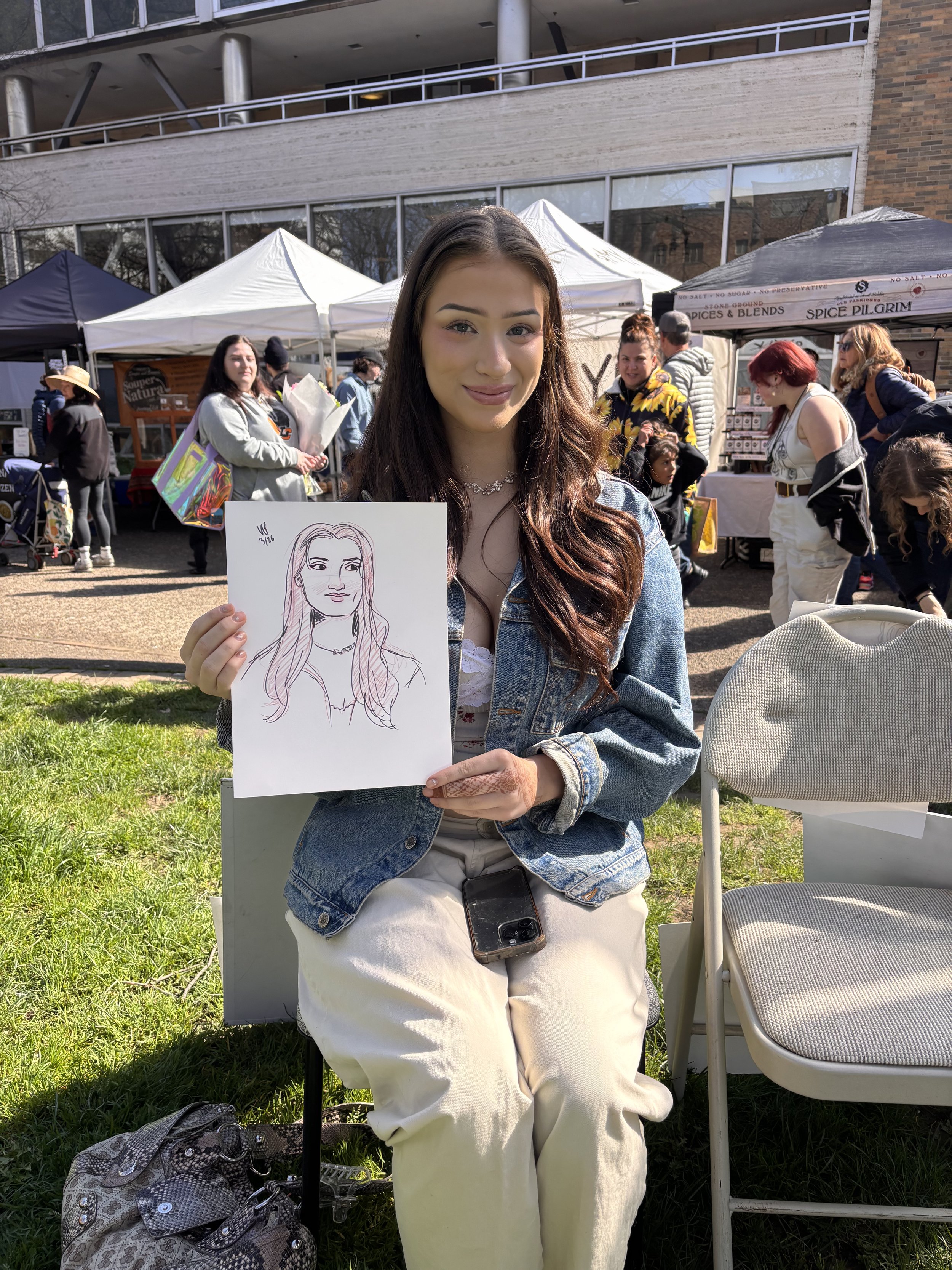 A young woman sitting with her live portrait drawing at the PSU Farmers Market.
