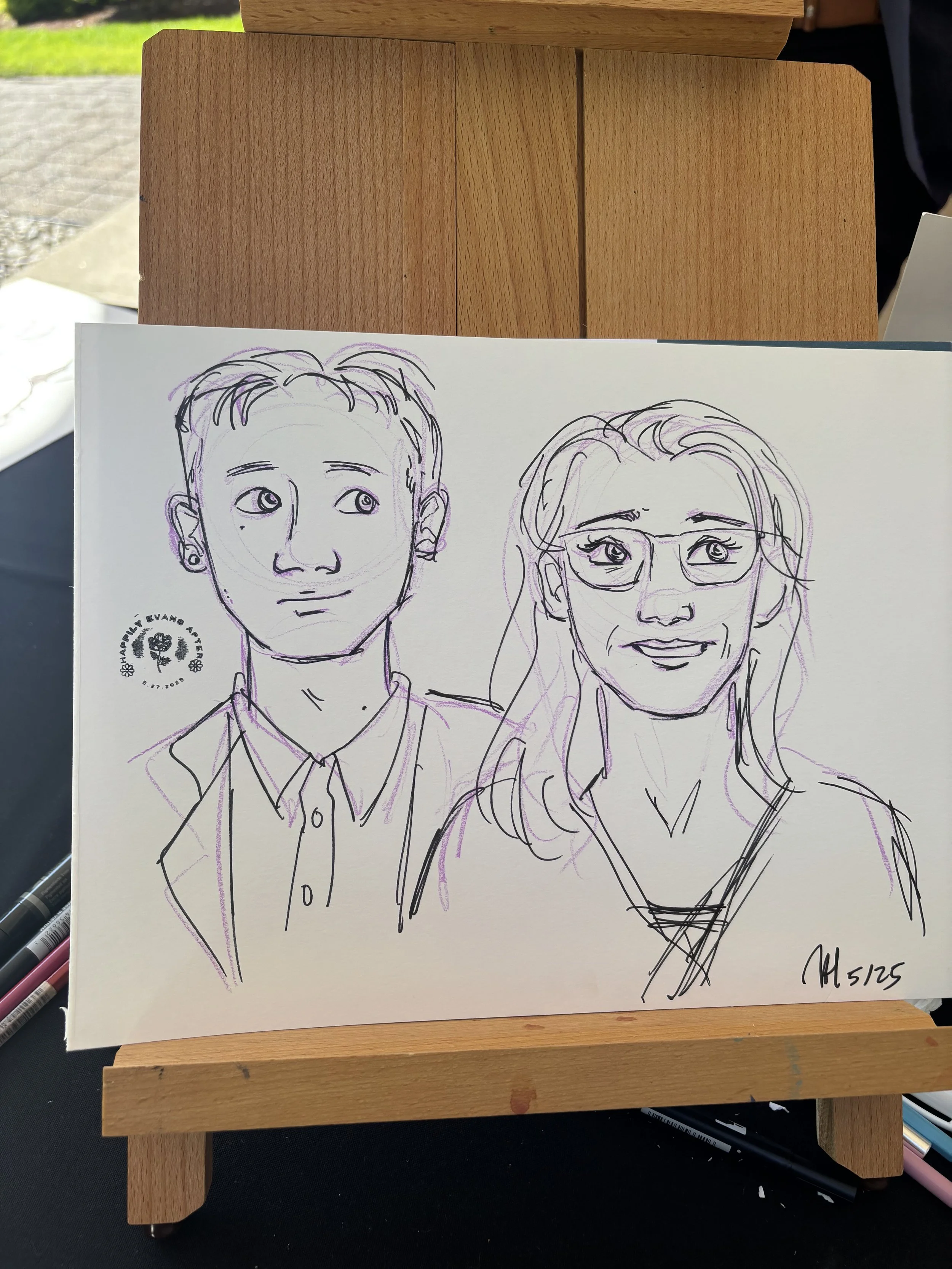 Sketch of a young man with short hair and a woman with glasses and long hair, both drawn with pen on paper, displayed on an easel.