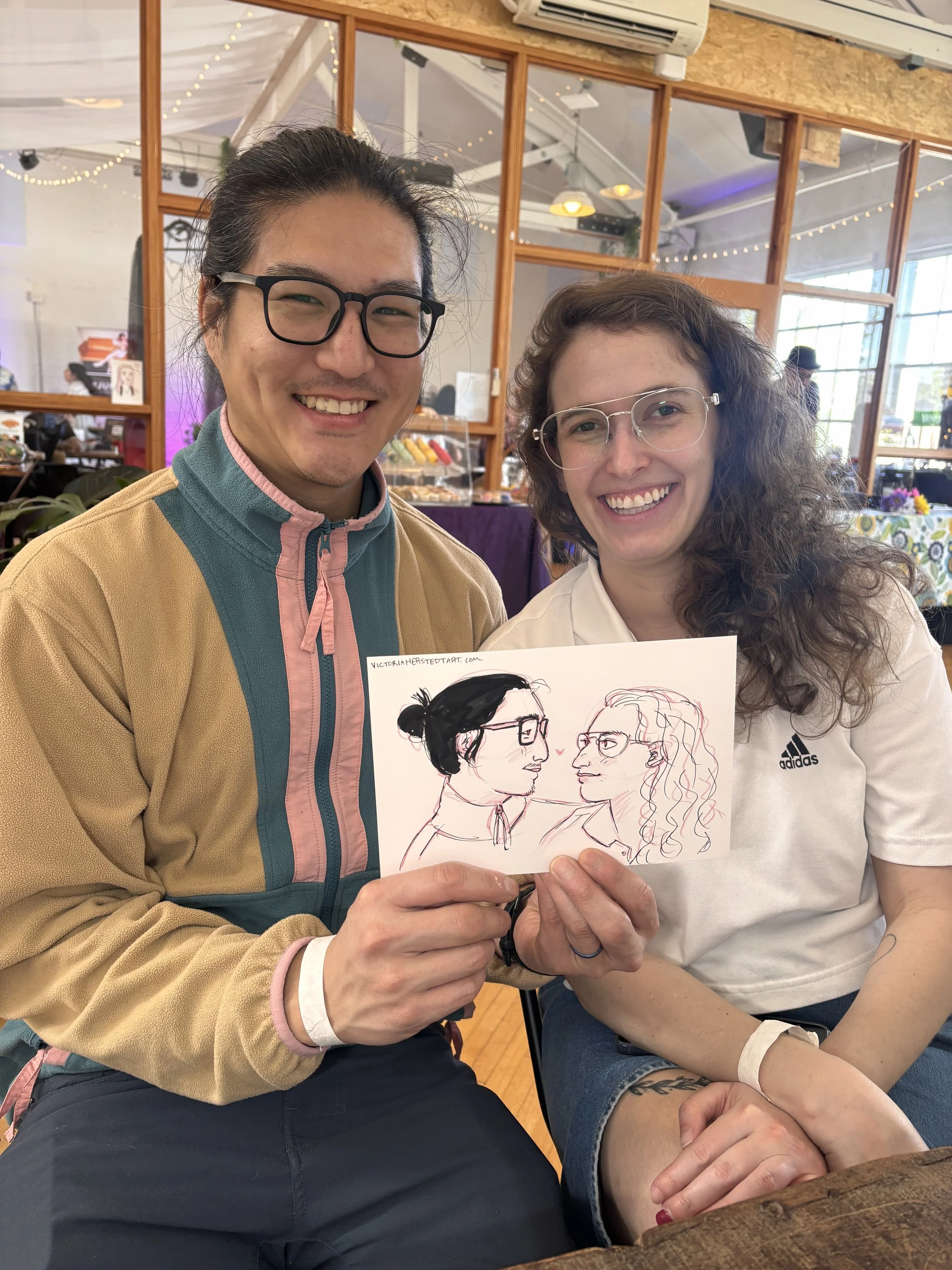 A couple holding their live portrait drawing at an alternative wedding expo.