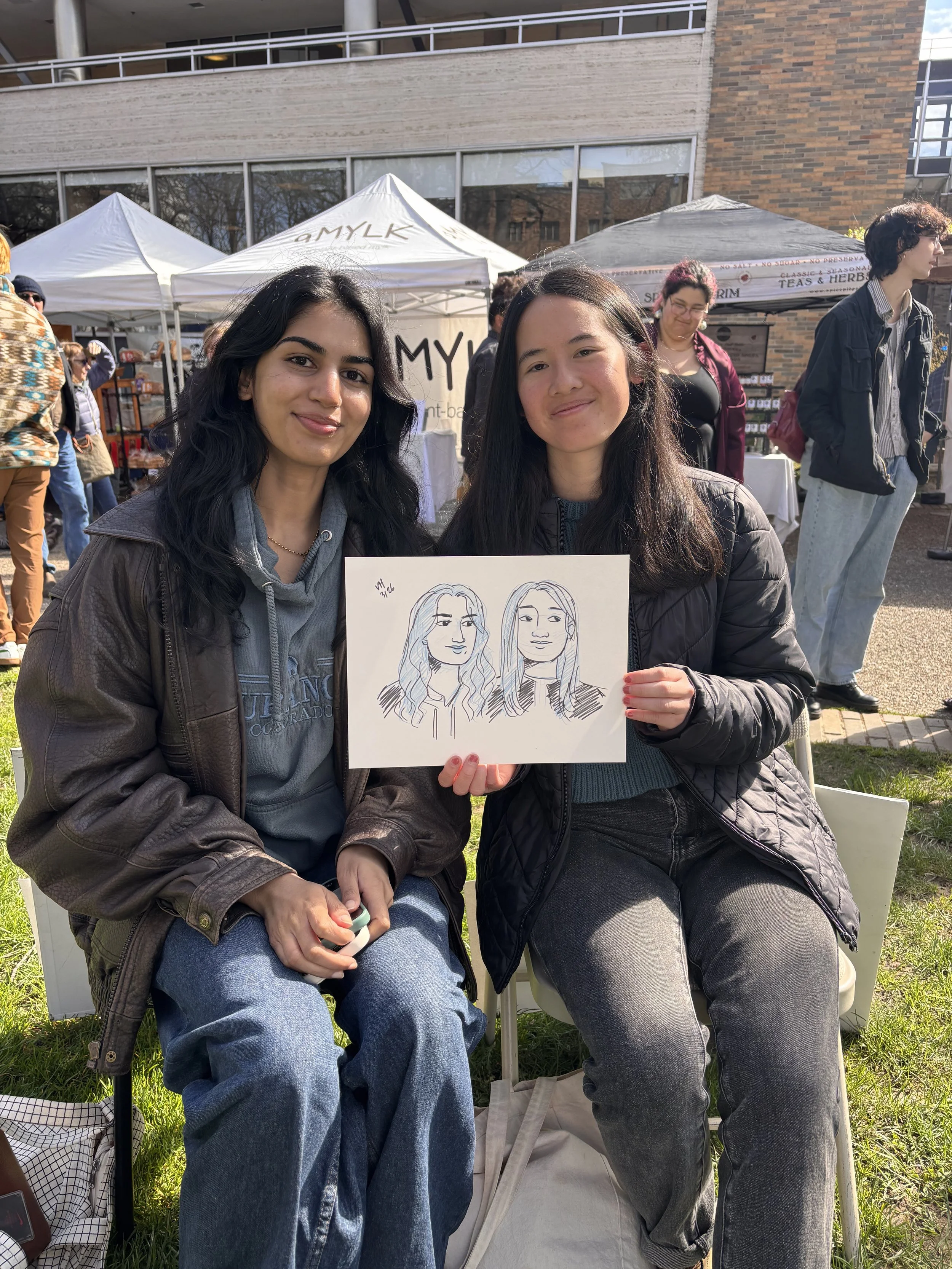 Two women sitting with their live portrait at the PSU Farmers Market.