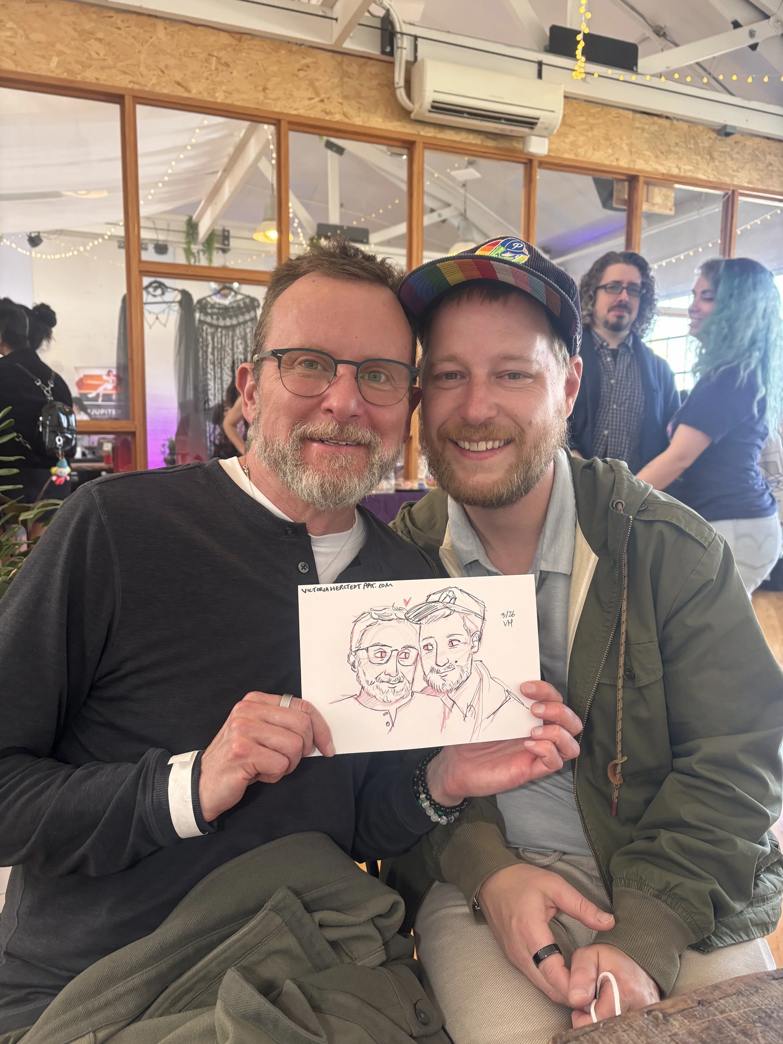 A gay male couple sitting with their live portrait drawing.