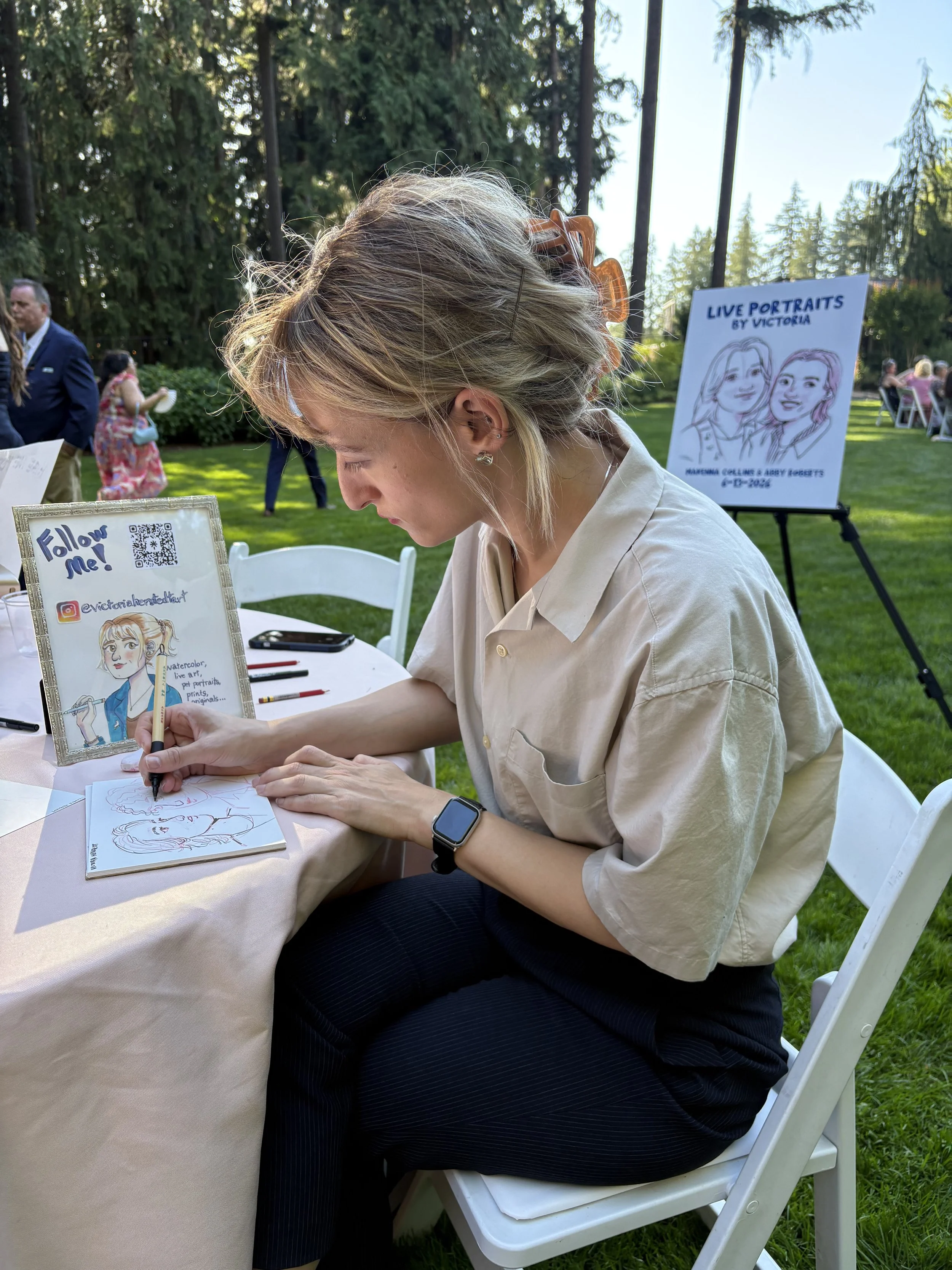 A live portrait artist working on a guest portrait at a wedding outside of two women, drawing with a felt marker pen.
