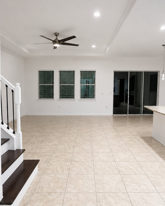 Empty living room with three windows, tiled floors, white walls, a ceiling fan, and a sliding glass door leading to another room.