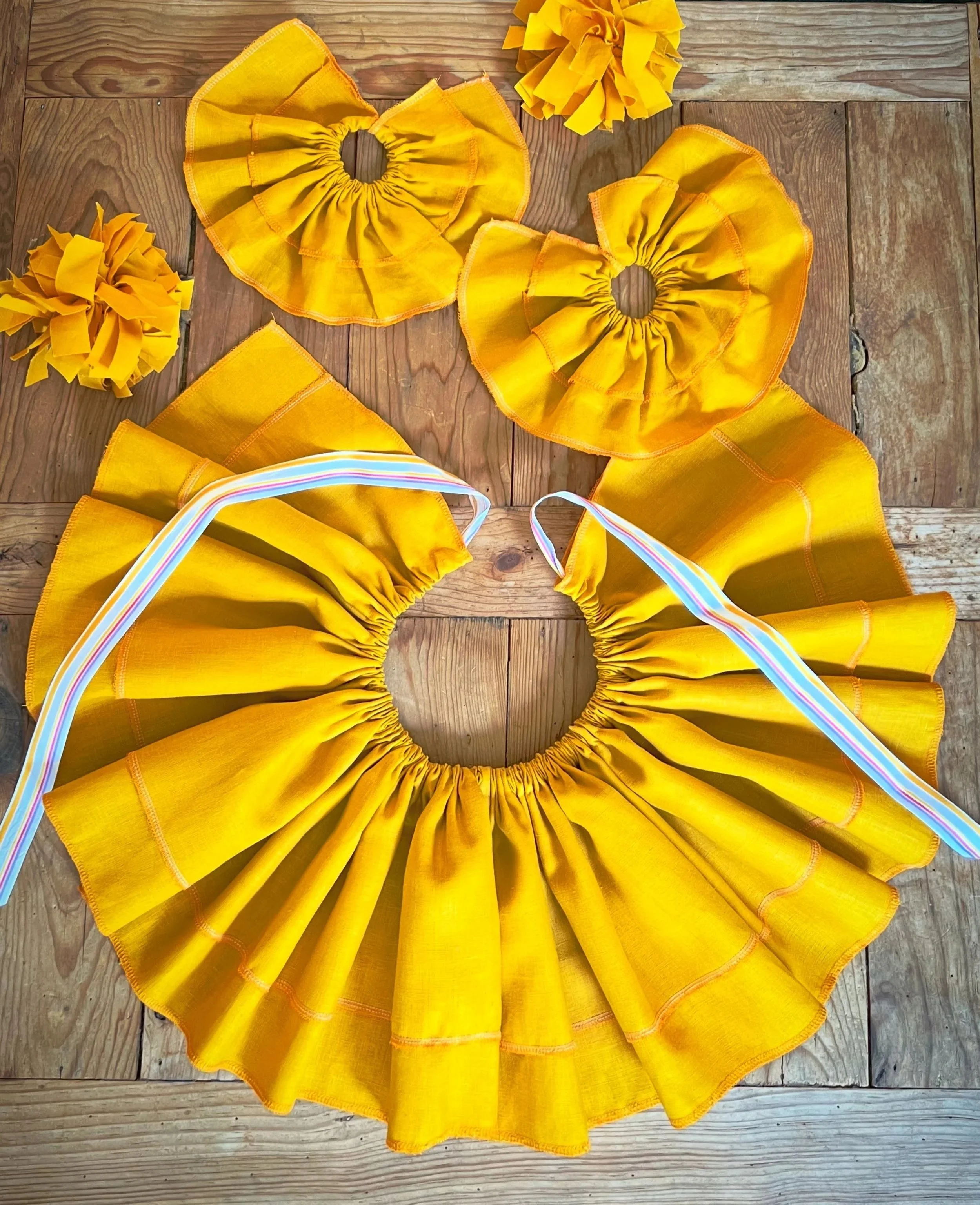 Bespoke handmade clown accessories, including yellow wrist ruffles, a ruffled yellow clown collar, displayed on a wooden background.