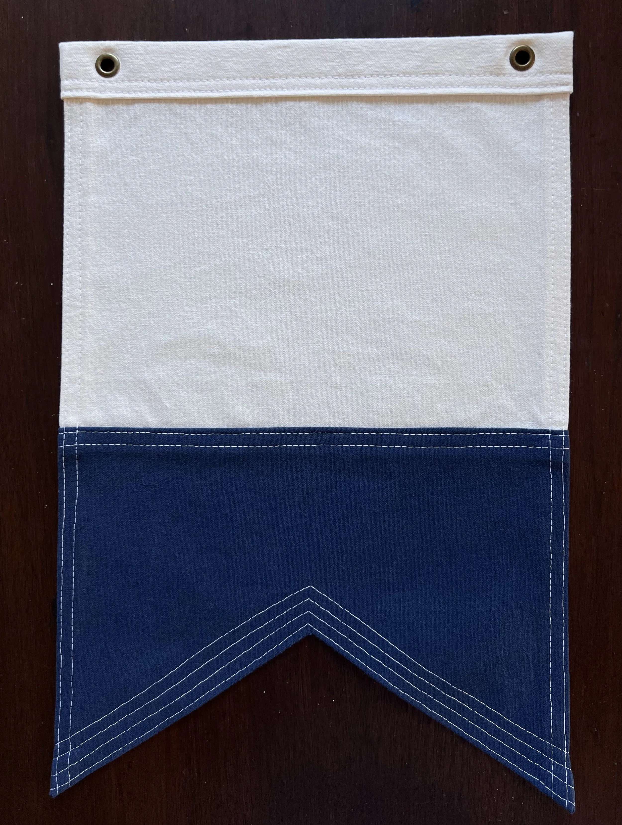 Nautical flag "A"  in navy blue and white with antique brass grommets at the top, hanging over a dark surface, with a blue fabric section at the bottom and a white fabric section at the top..