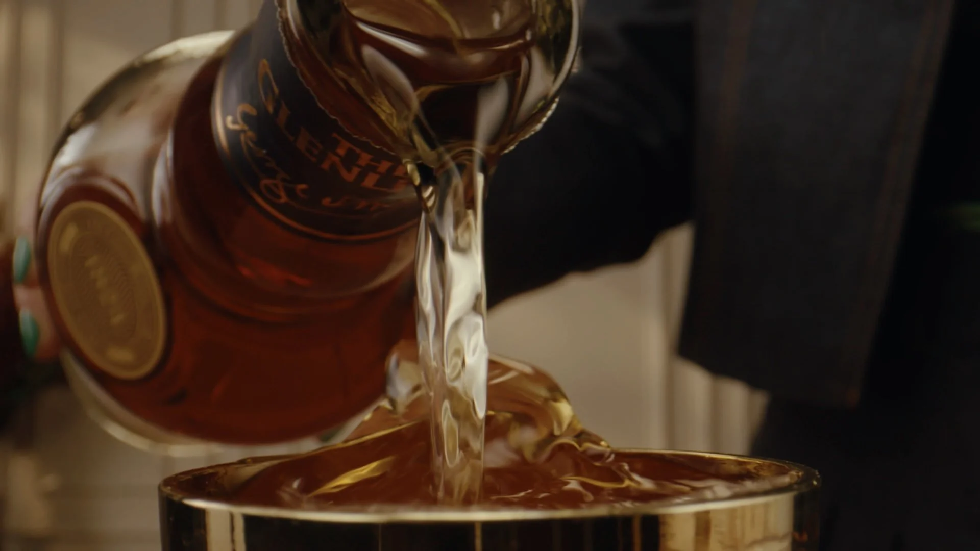 A person pouring a bottle of liquor into a glass container.