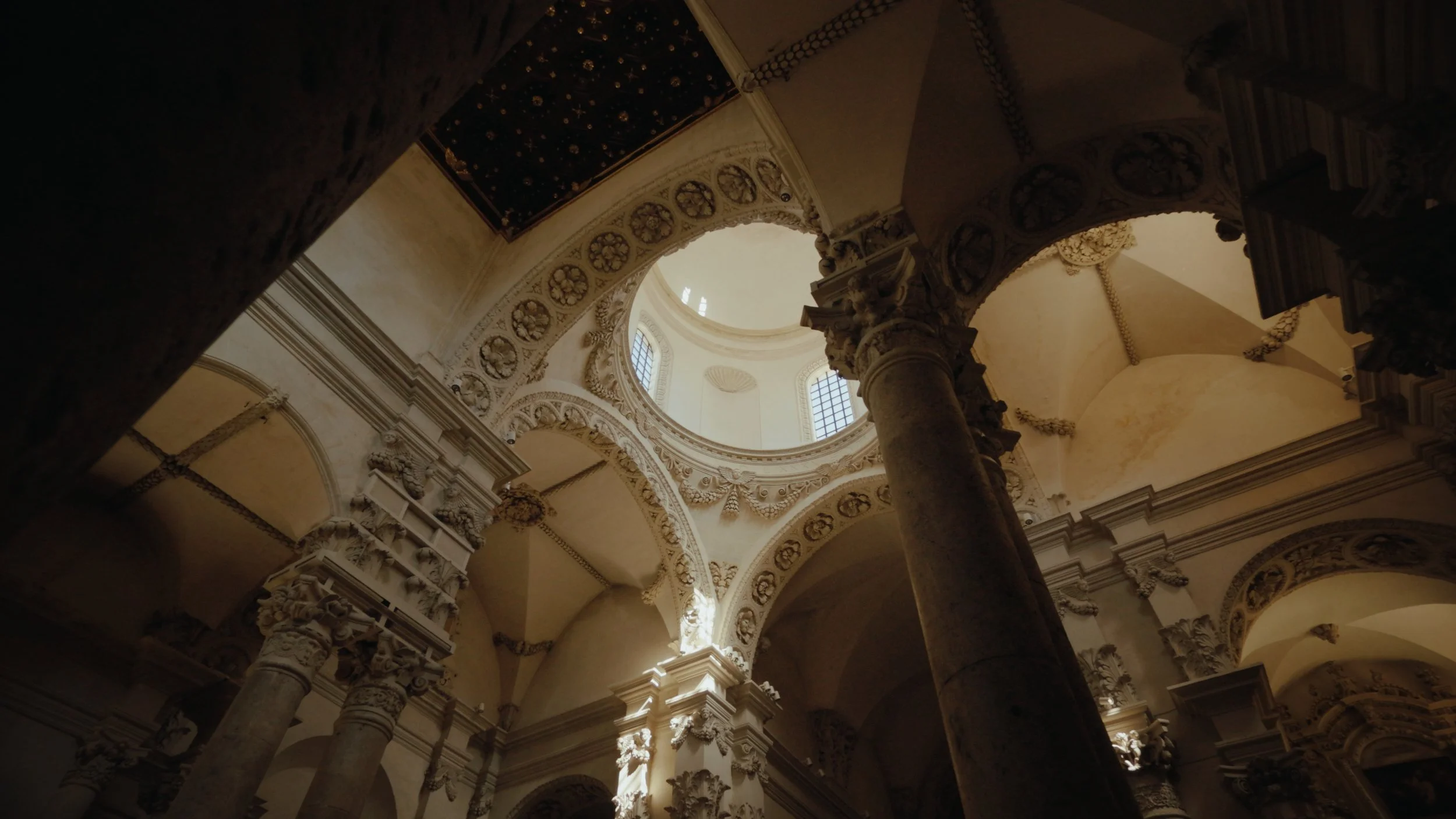 Interior view of a historic church or cathedral with ornate arches, columns, and a domed ceiling with windows allowing natural light to enter.