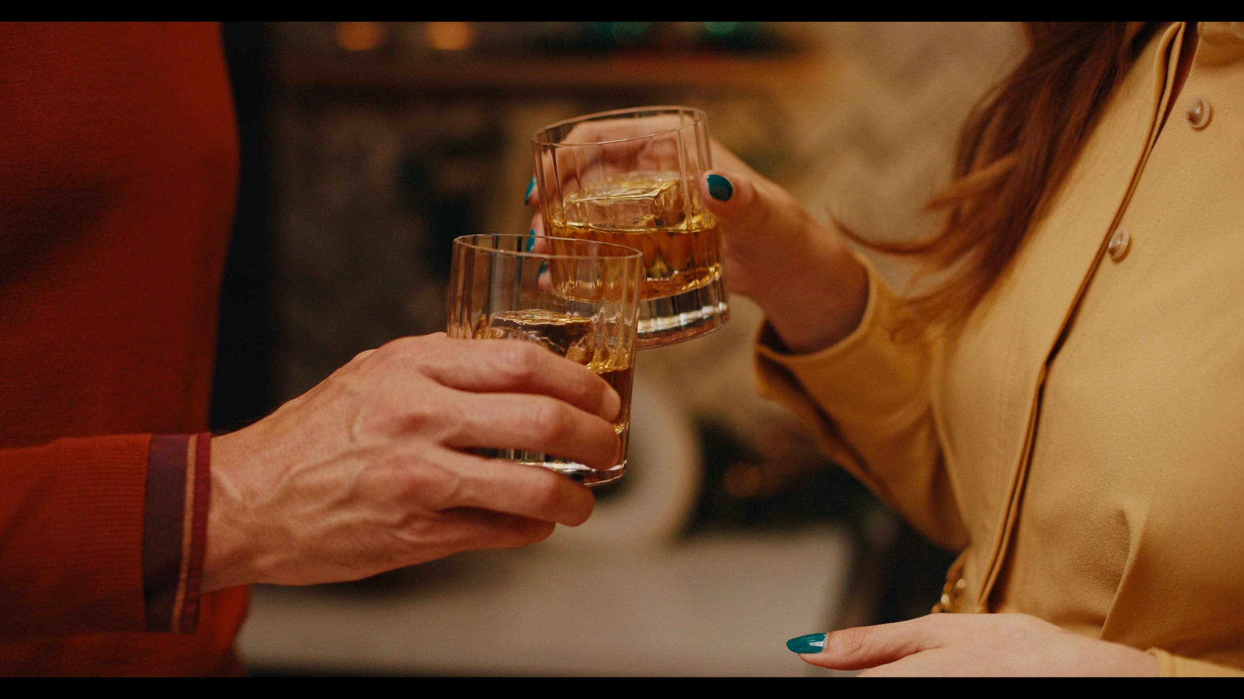Two women clinking glasses of whiskey with ice in a toast during a social gathering.