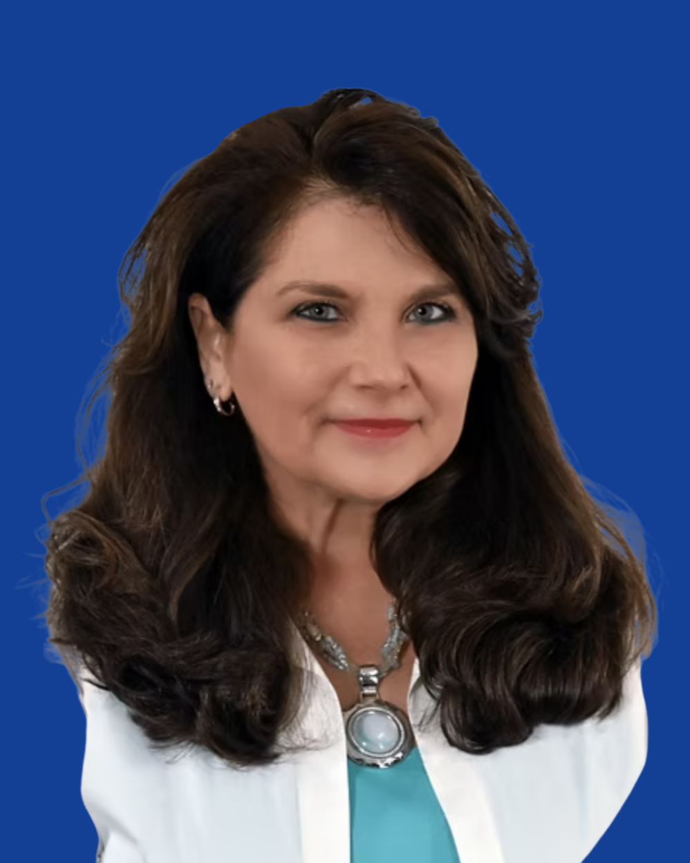 Close-up of a woman with long, wavy brown hair and blue eyes, wearing jewelry including a necklace with a large turquoise pendant and earrings, against a light background.