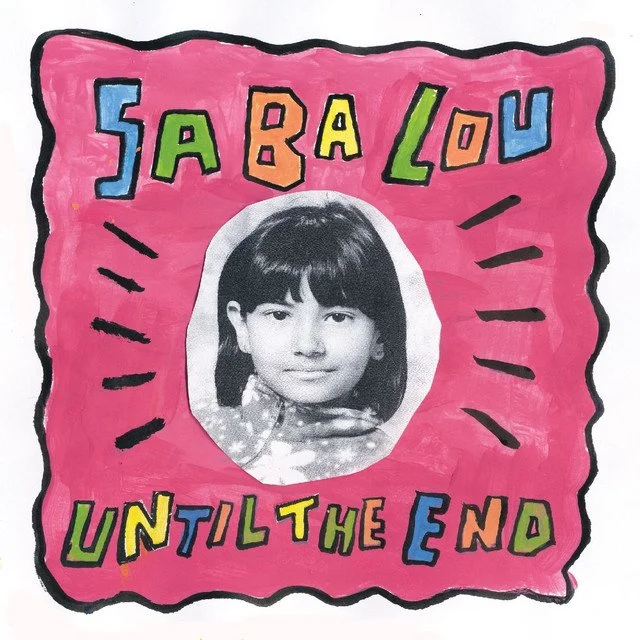Colorful handmade poster with a black-and-white photo of a girl with dark hair and bangs at the center. The background is pink with a wavy black border. The words "SARAH LOVES UNTIL THE END" are written in large, colorful letters around the photo. Black lines radiate outward from the photo, emphasizing the central image.