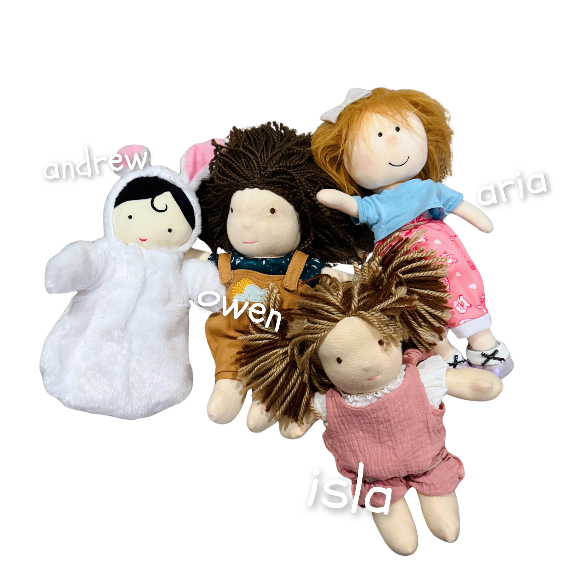 Several plush dolls lying on a surface, including a girl with long dark hair, a girl with curly brown hair, a girl with straight light brown hair, and a girl with long auburn hair. The dolls are arranged with some overlapping.