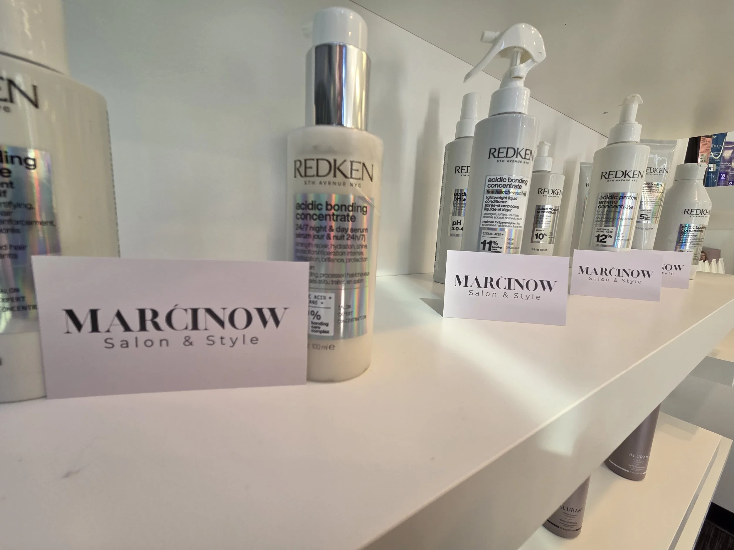 Display of Redken hair care products on a white salon shelf with Marcinow Salon & Style labels in front of each product.