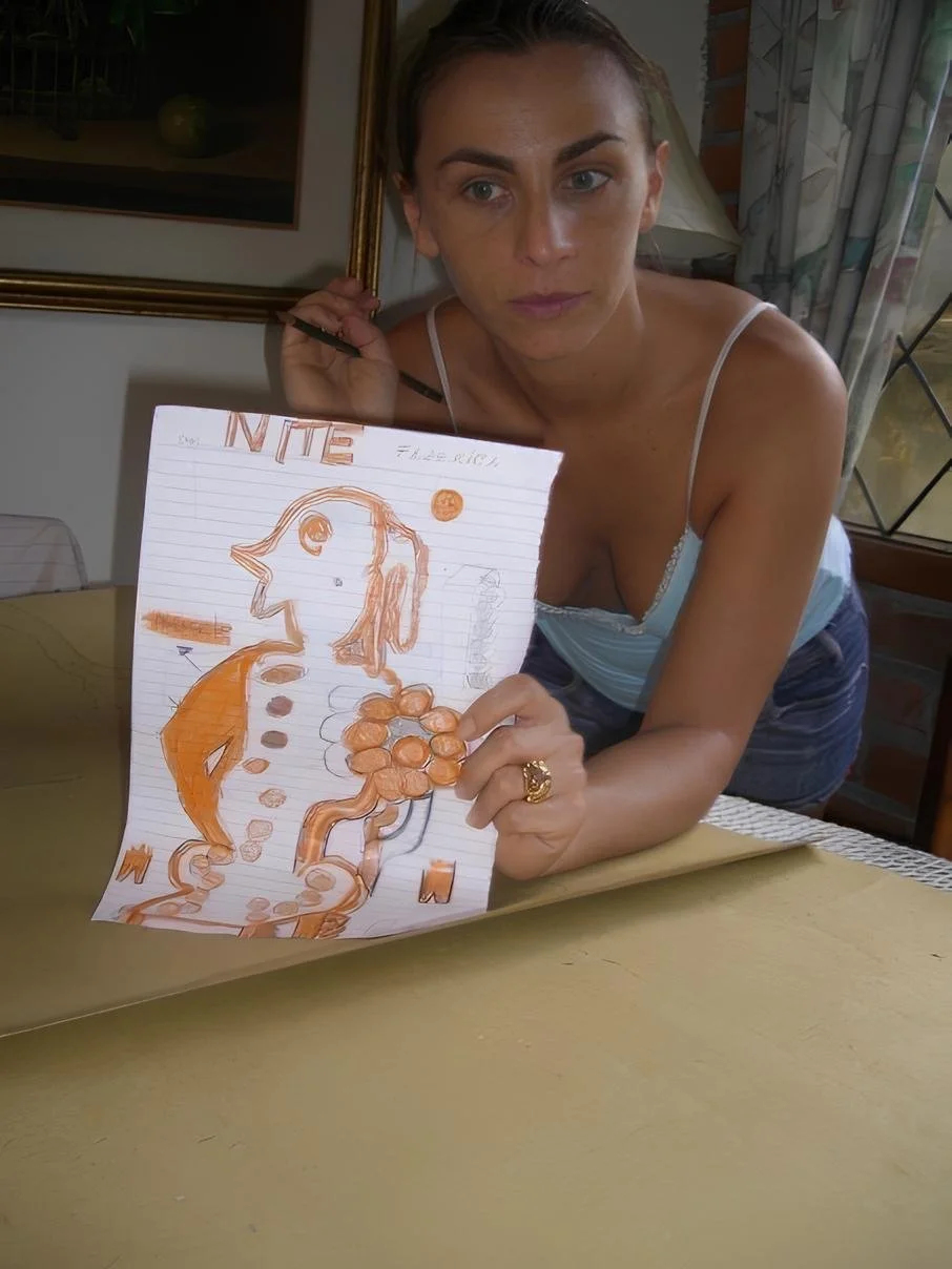 Woman holding a drawing of a dog with orange and black markers on a lined sheet of paper, sitting at a yellow table.