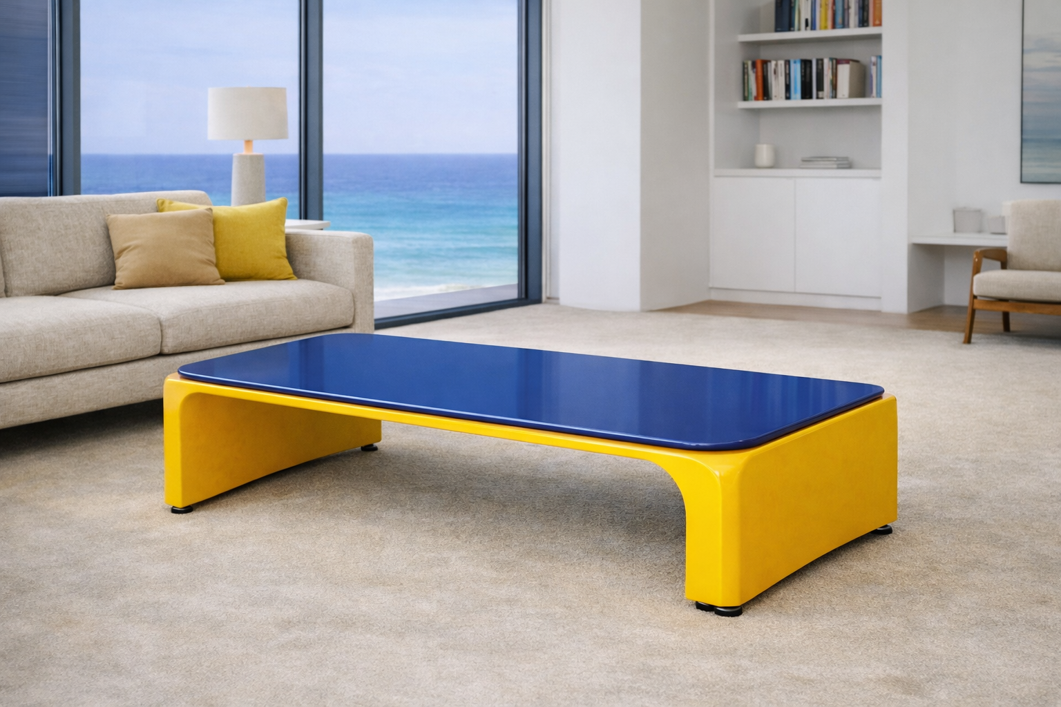 Living room with beige couch, yellow pillows, blue and yellow coffee table, large glass door showing ocean view, white bookshelf, and armchair.