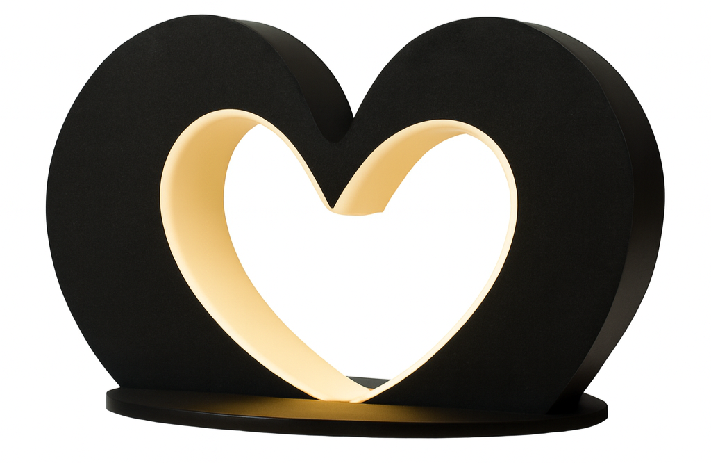 A black heart-shaped lamp with a glowing white heart inside it, resting on a flat base