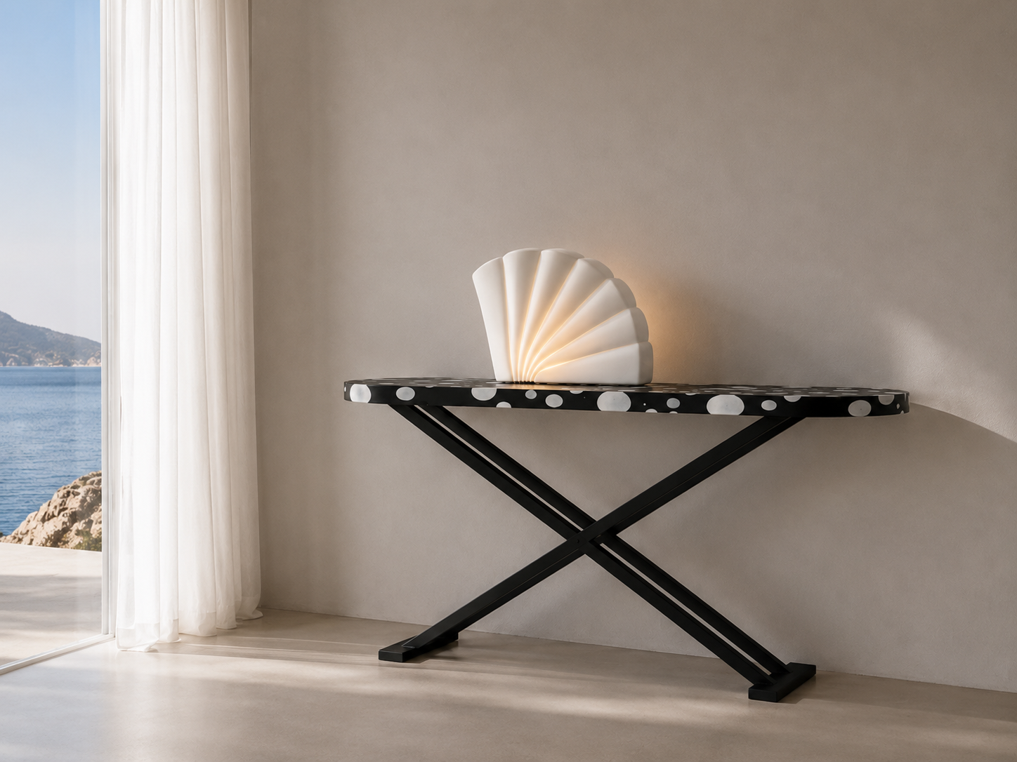 Decorative black console table with white polka dots, placed against a plain wall, with a white accordion-style lamp and a wall-mounted light behind it, near a window showing a view of water and mountains outside.