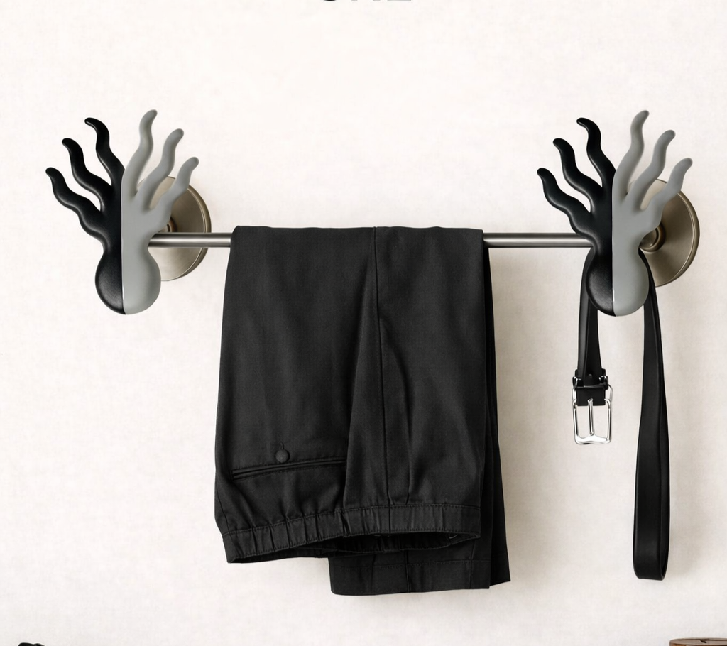 A wall hook with black and gray hands-shaped grips holding a pair of black pants and a black belt.