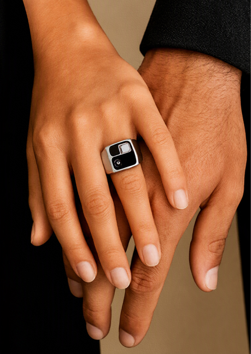 Close-up of two hands gently holding each other with one hand wearing a large silver ring with a black and silver design.
