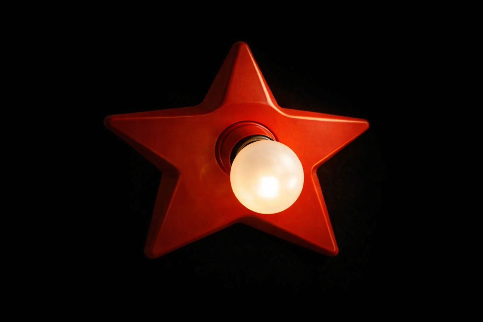 Red star-shaped light fixture with a glowing white bulb in the center, set against a black background.