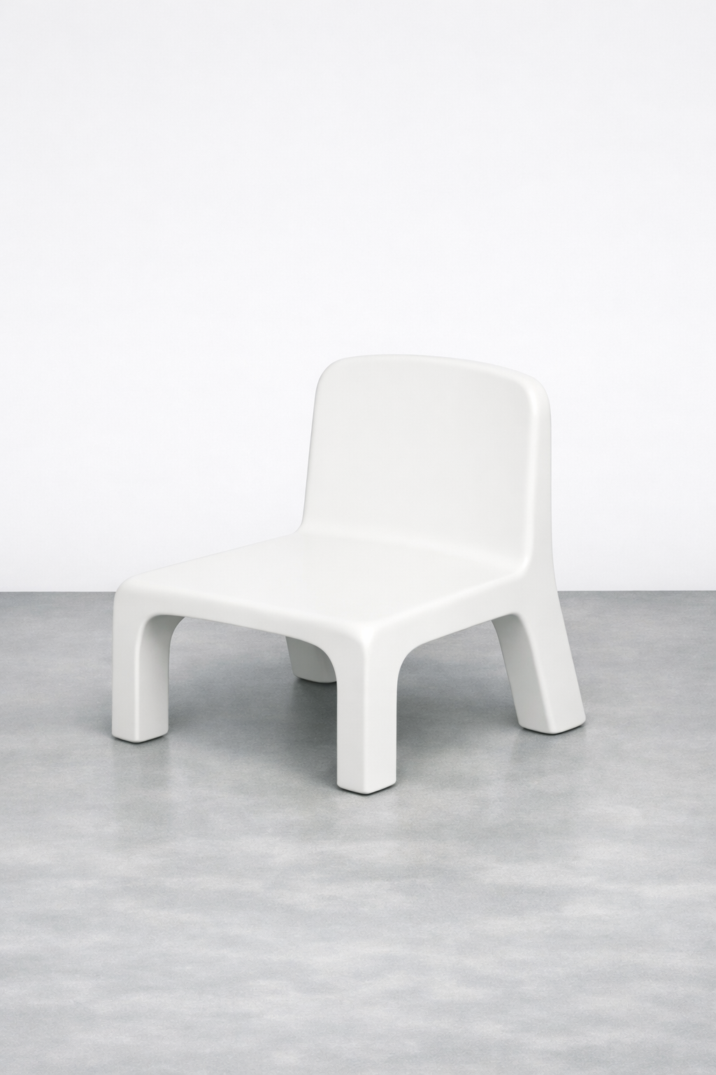 A modern white plastic chair with four chunky legs on a gray floor against a plain white wall.
