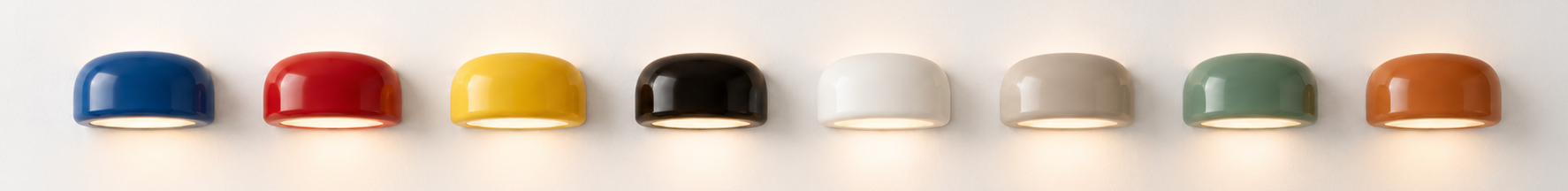 Collection of seven colorful dome-shaped wall lamps in blue, red, yellow, black, white, green, and orange mounted on a white wall.