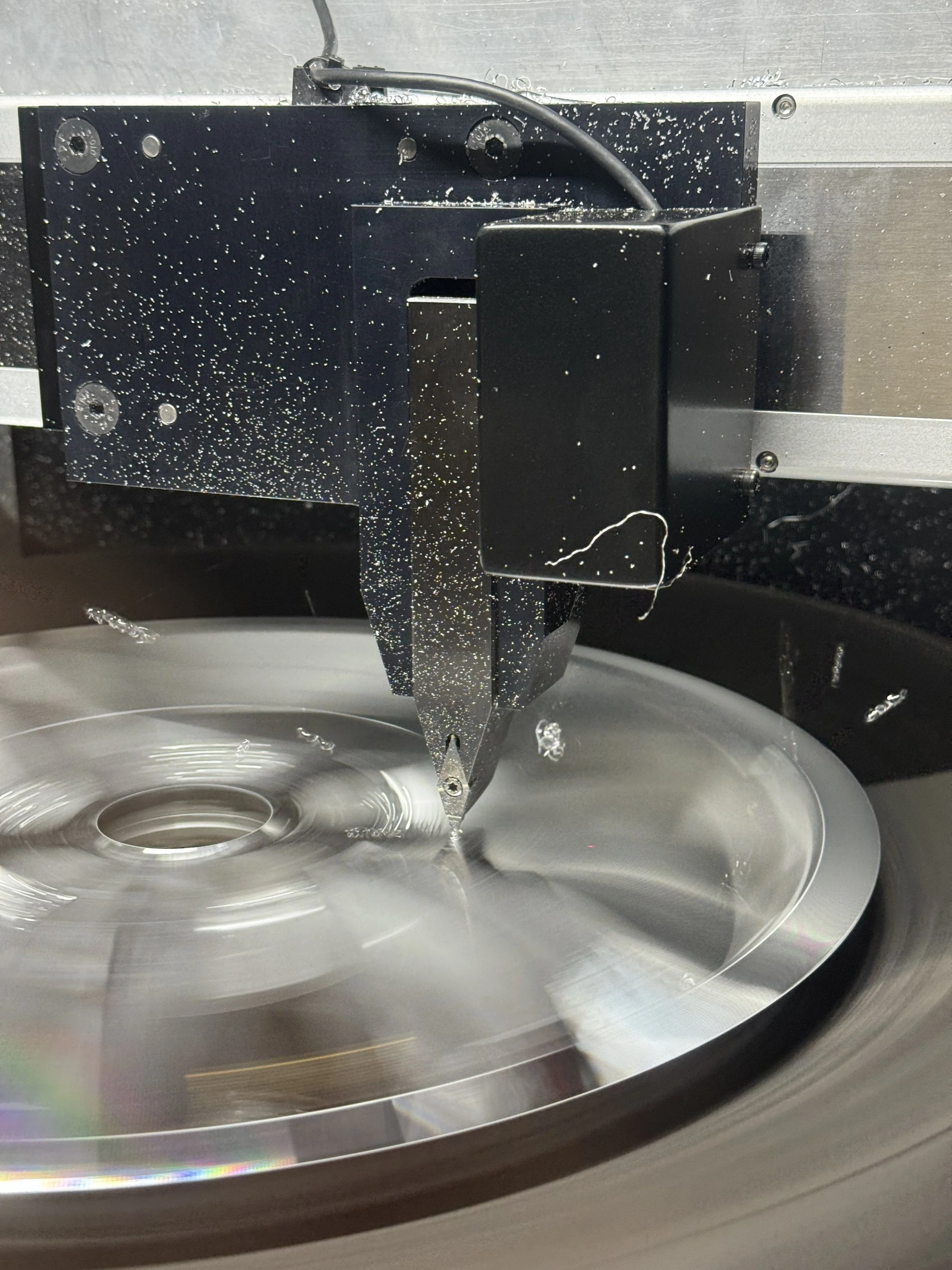 Close-up of a CNC machine cutting or engraving a metal disc with a spinning blade.