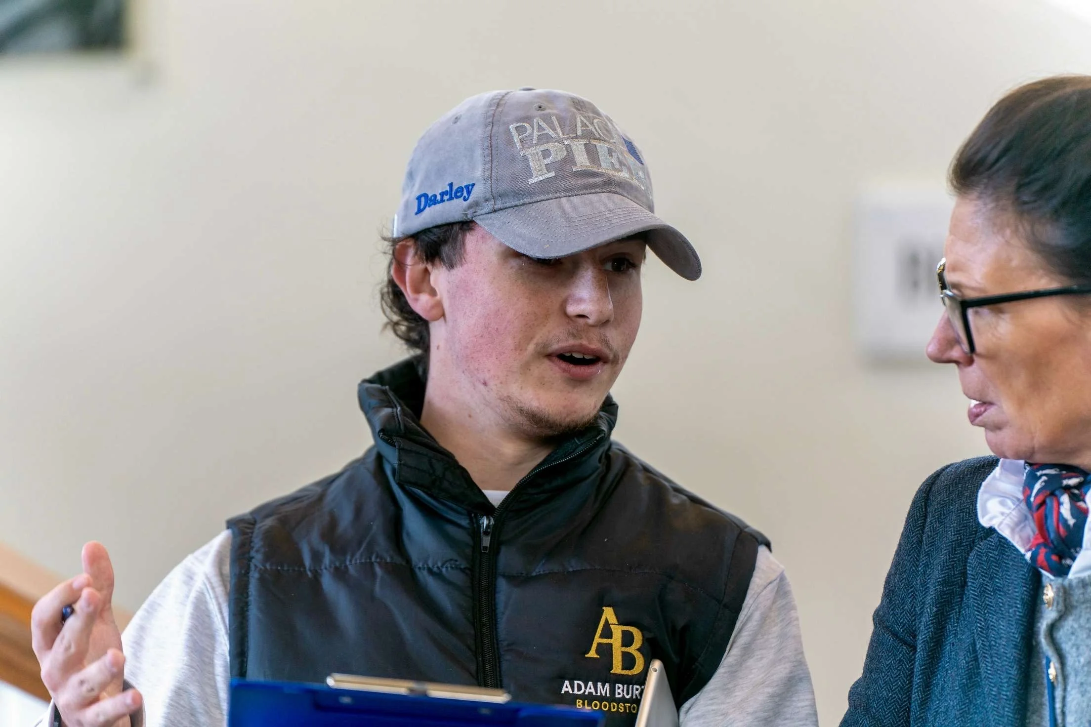 A young man with a cap engaged in a conversation with a person wearing glasses.