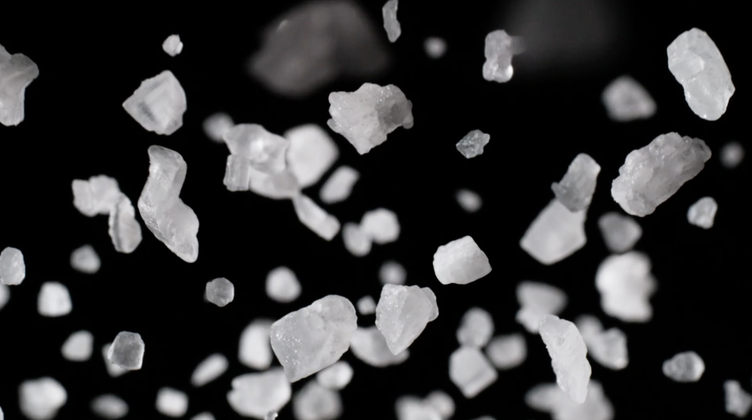Close-up of numerous white salt crystals falling against a black background.