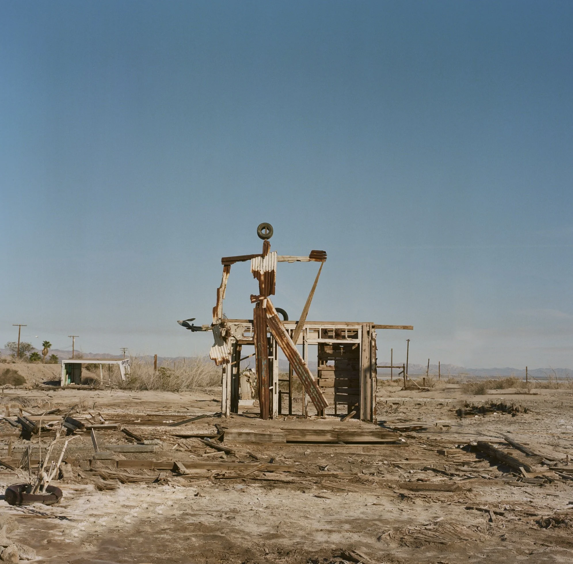 Remains of a destroyed wooden structure with rubble and debris scattered on the ground, under a clear blue sky.