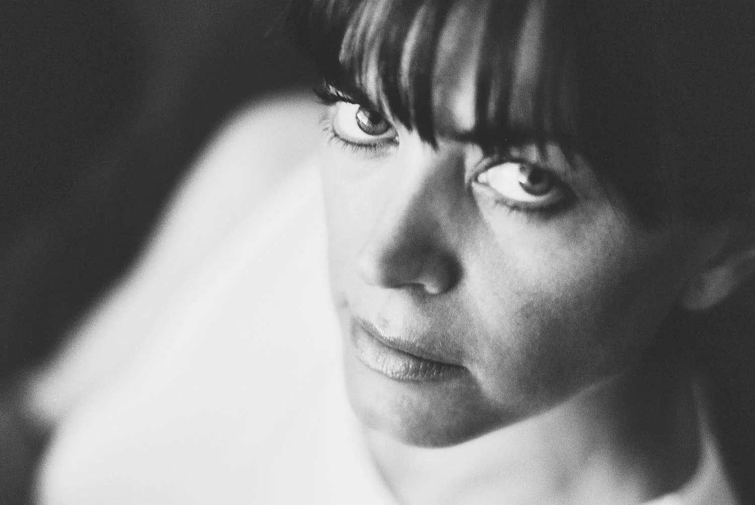 Black and white close-up portrait of a person with short dark hair and expressive eyes, gazing directly into the camera.