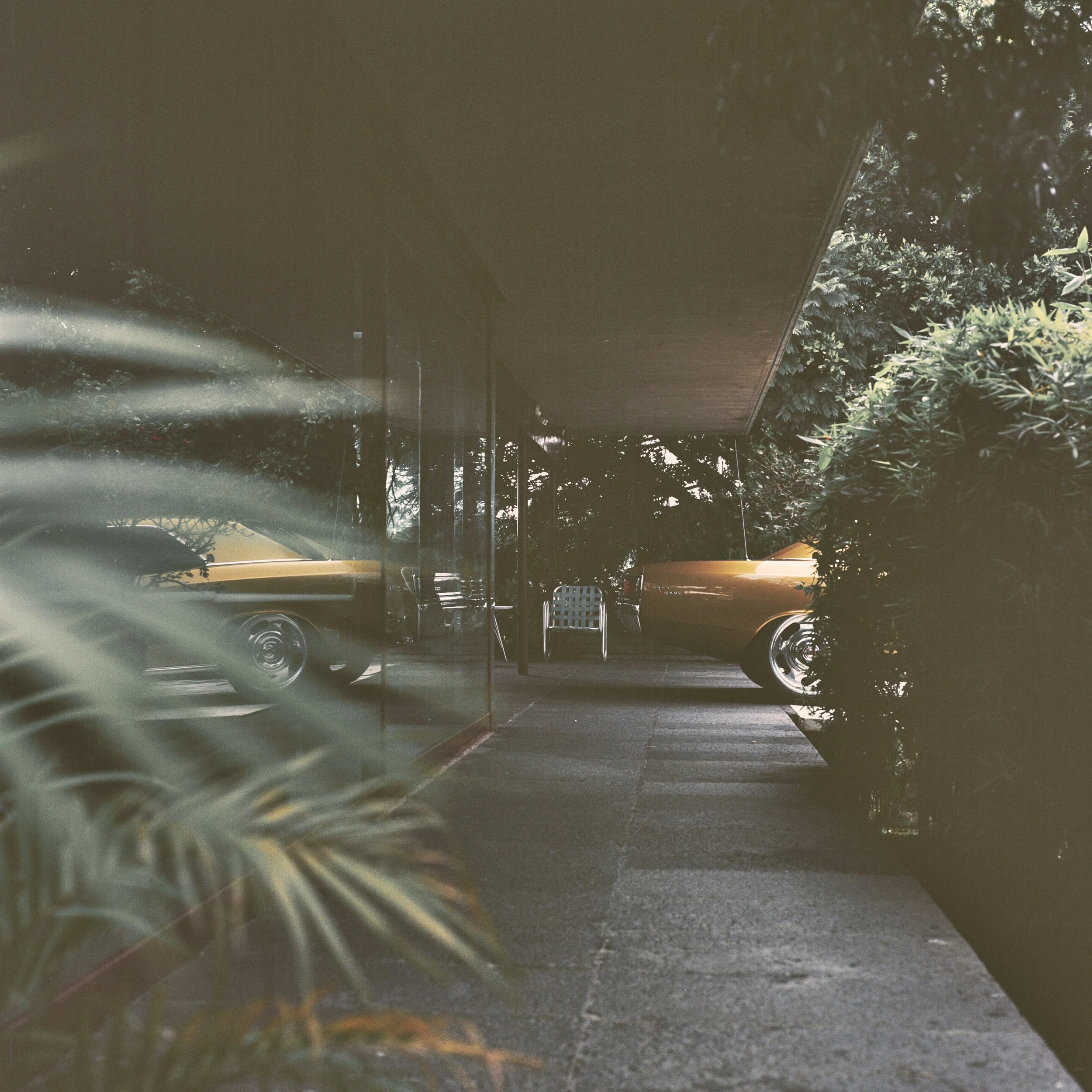 A view of a parking lot under a bridge with cars parked and greenery on the sides, seen from inside a vehicle.