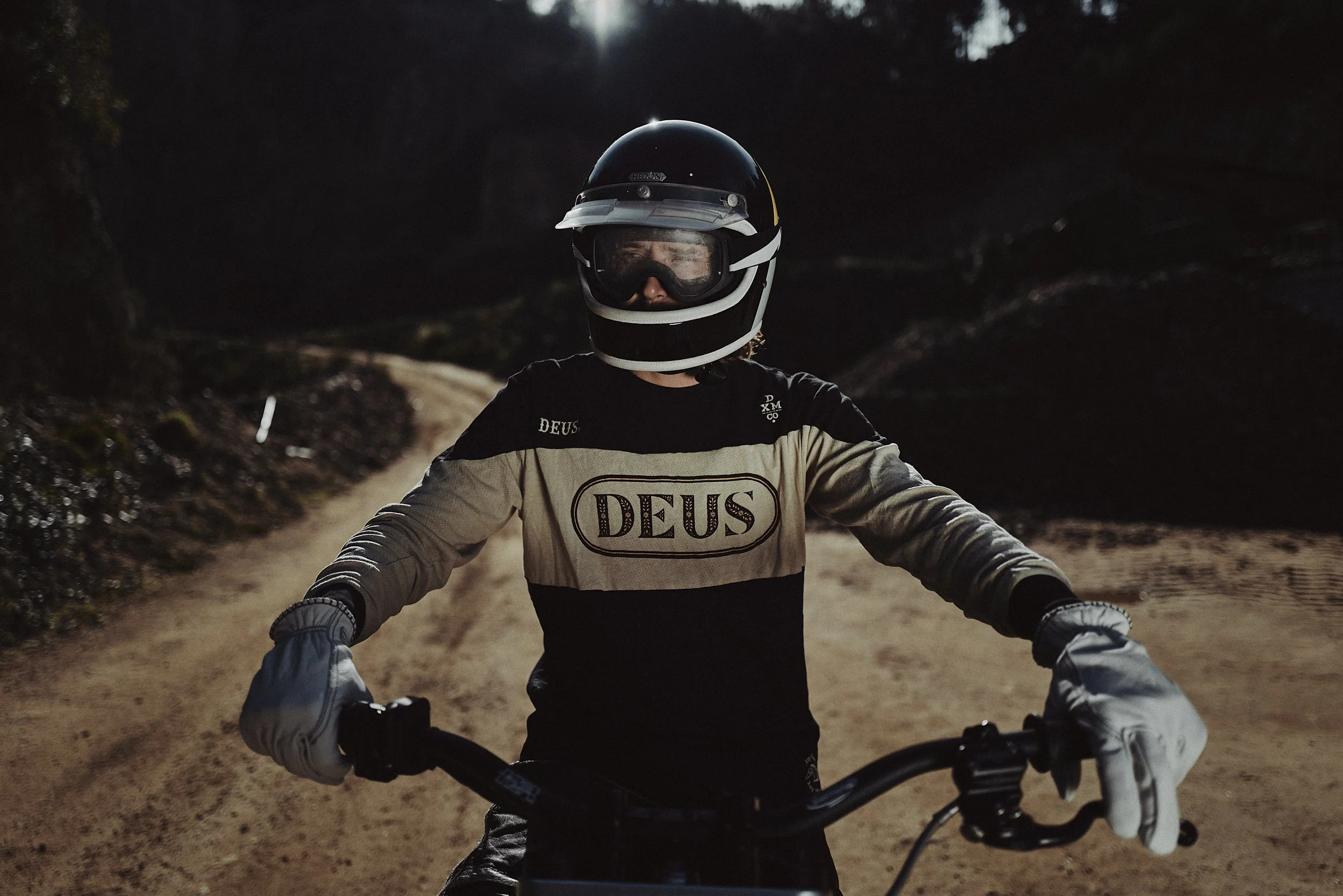 A person wearing a motorcycle helmet and gloves, riding a dirt bike on a trail at night with a dark background.