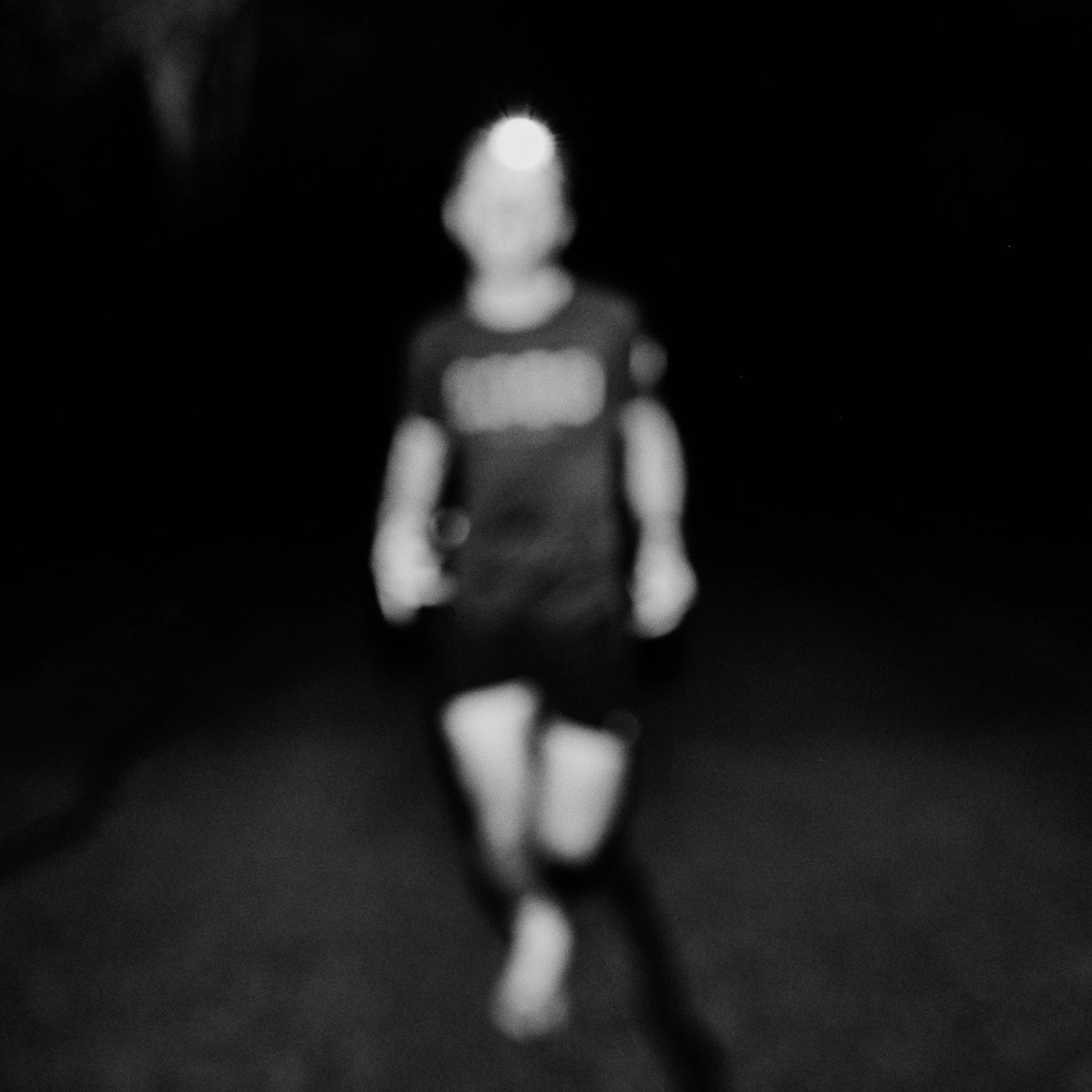 A blurred black-and-white photo of a small figurine or object with a bright light source behind it, creating a silhouette in a dark environment.