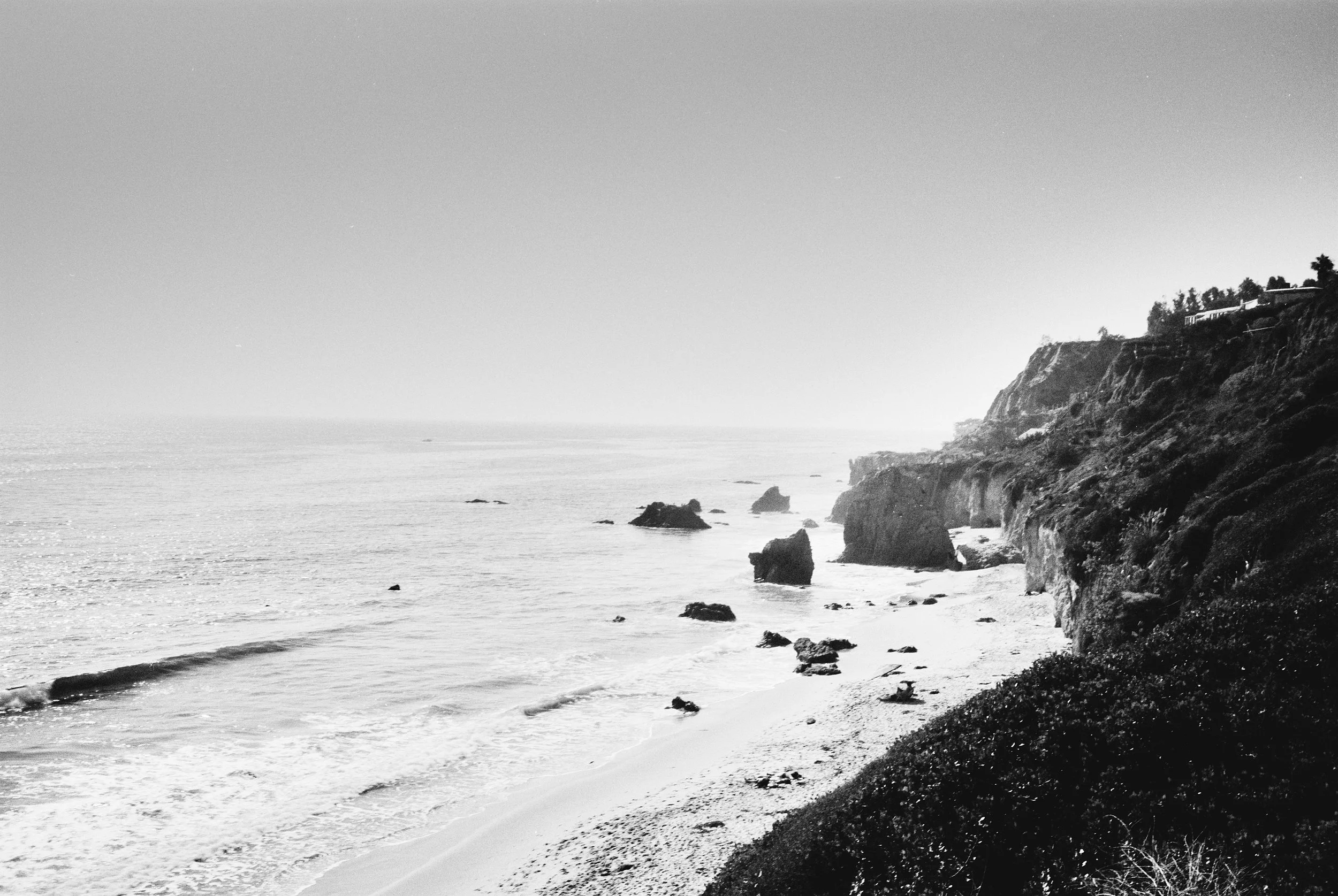 A black and white photo of a coastal landscape with cliffs and the ocean, and a few houses on the cliffs.
