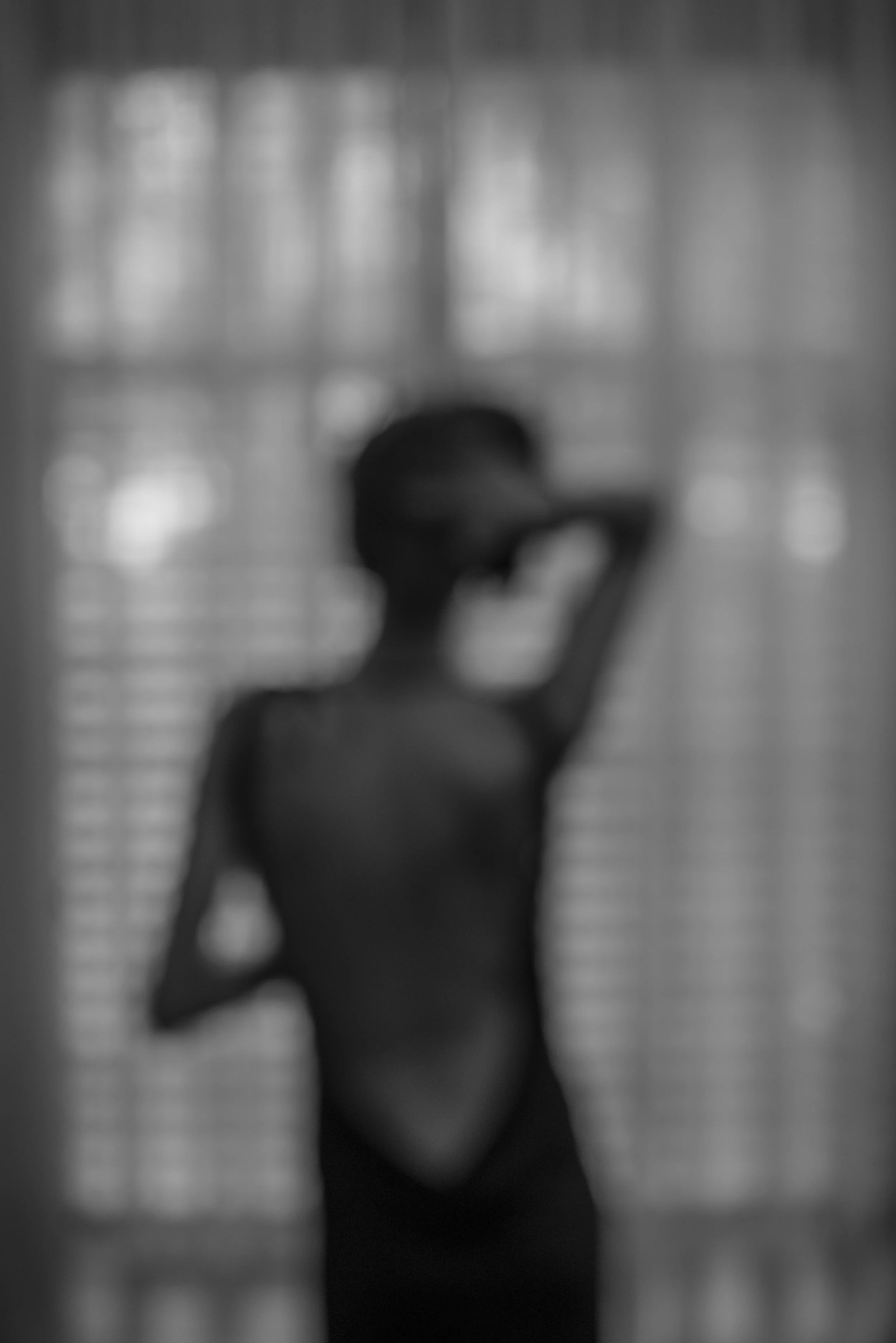 A blurred, black-and-white photograph of a woman in a hat, holding a phone to her ear, with a background of blurred, lit-up windows or light panels.