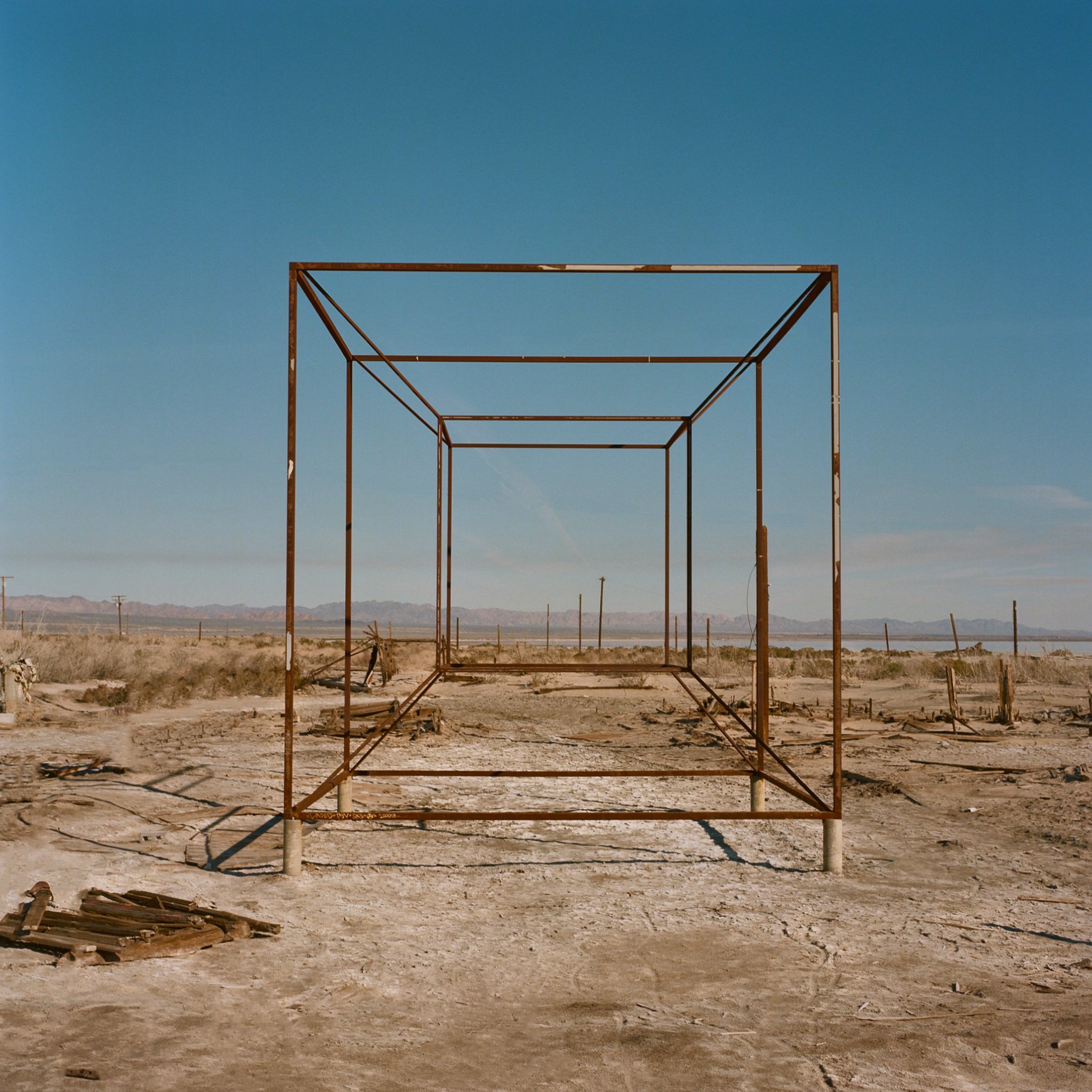 Empty metal framework structure in a desert landscape with mountains in the background and a clear blue sky.