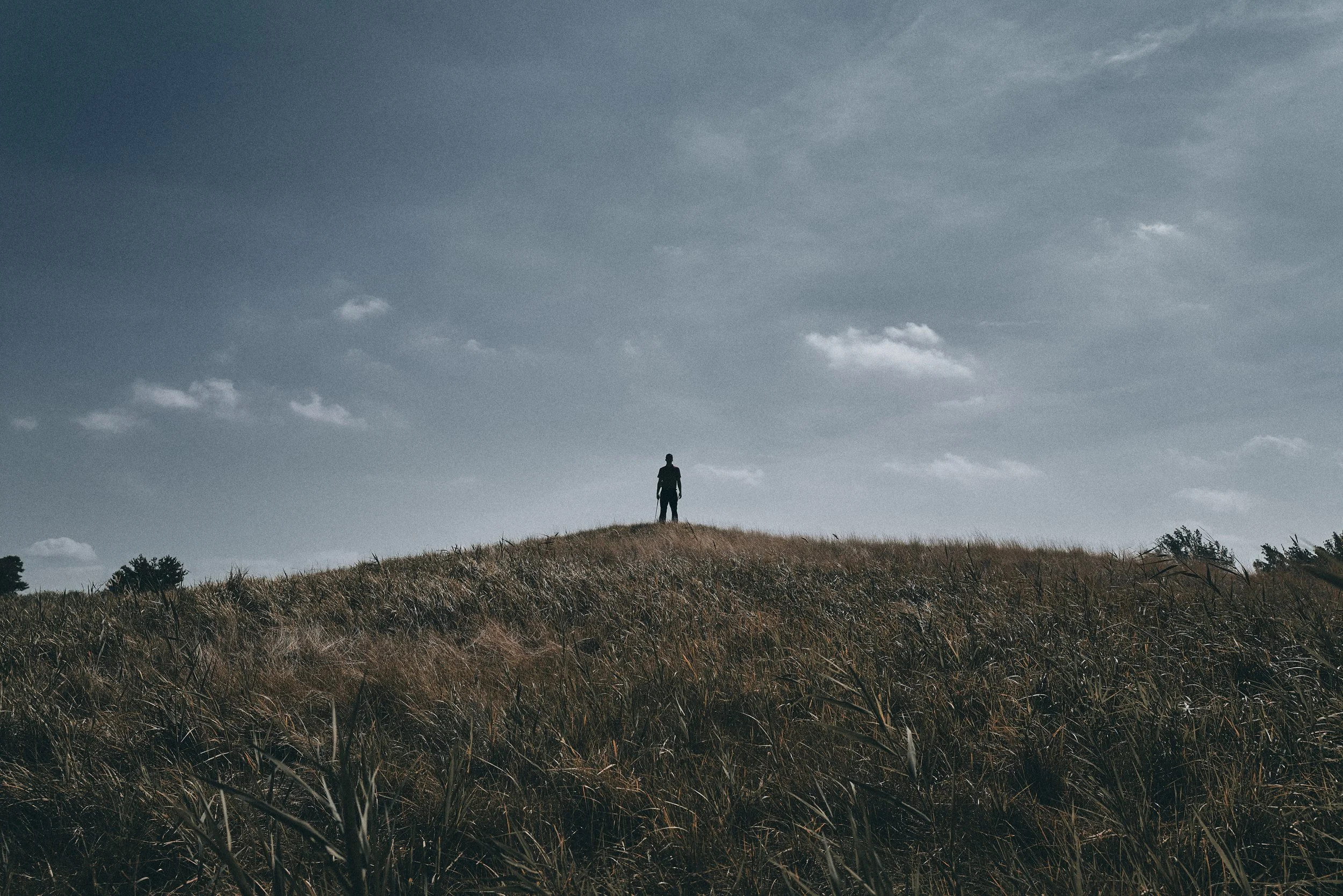 A person stands alone on a grassy hill under a cloudy sky.