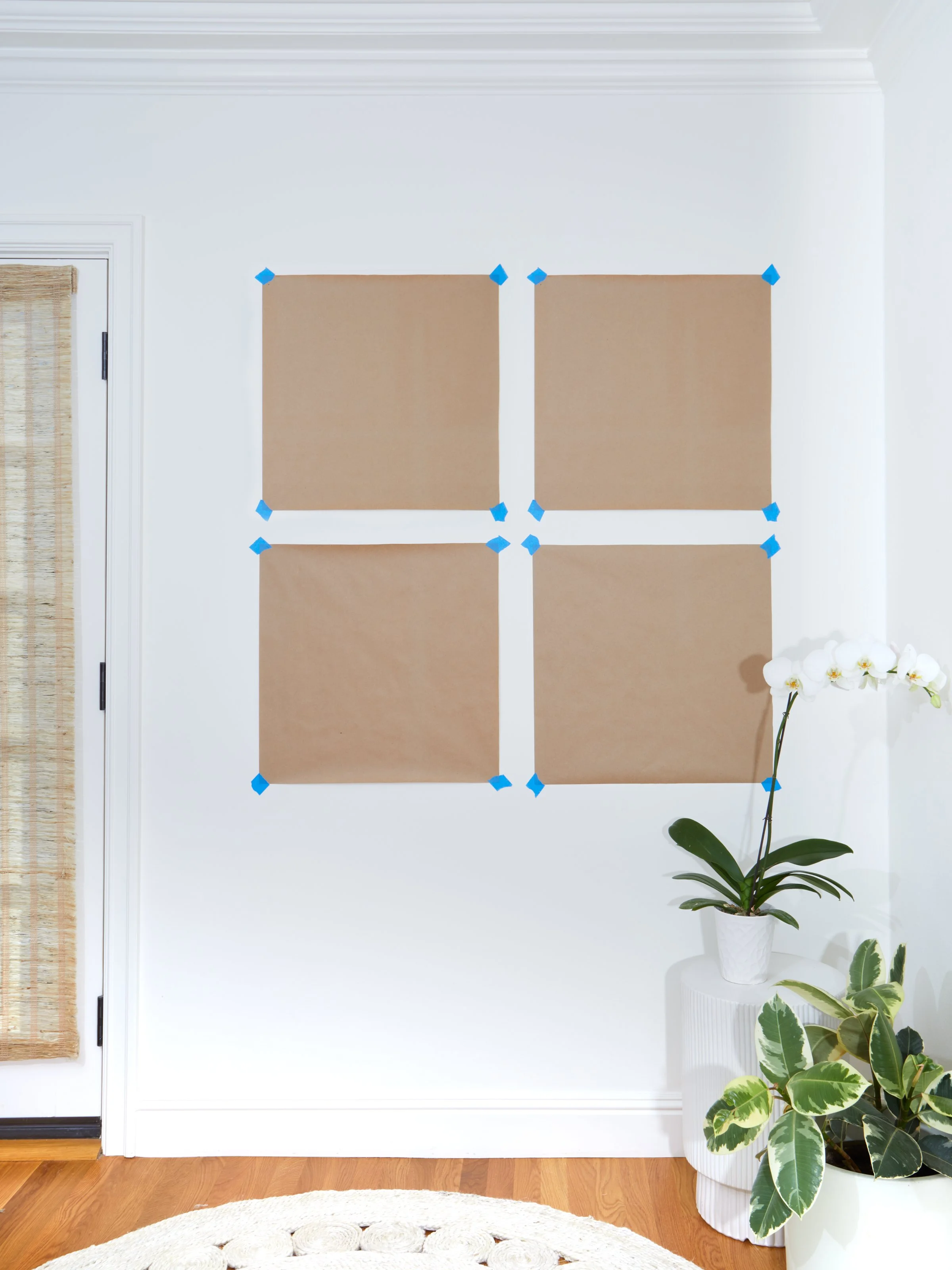 Before photo showing four kraft paper templates taped to a white wall to plan a symmetrical gallery wall layout before hanging frames