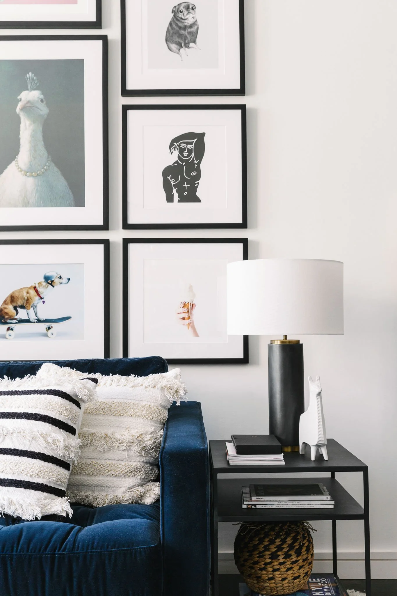 Eclectic gallery wall with black frames featuring a dog on skateboard print and abstract photography above a blue velvet sofa with textured pillows