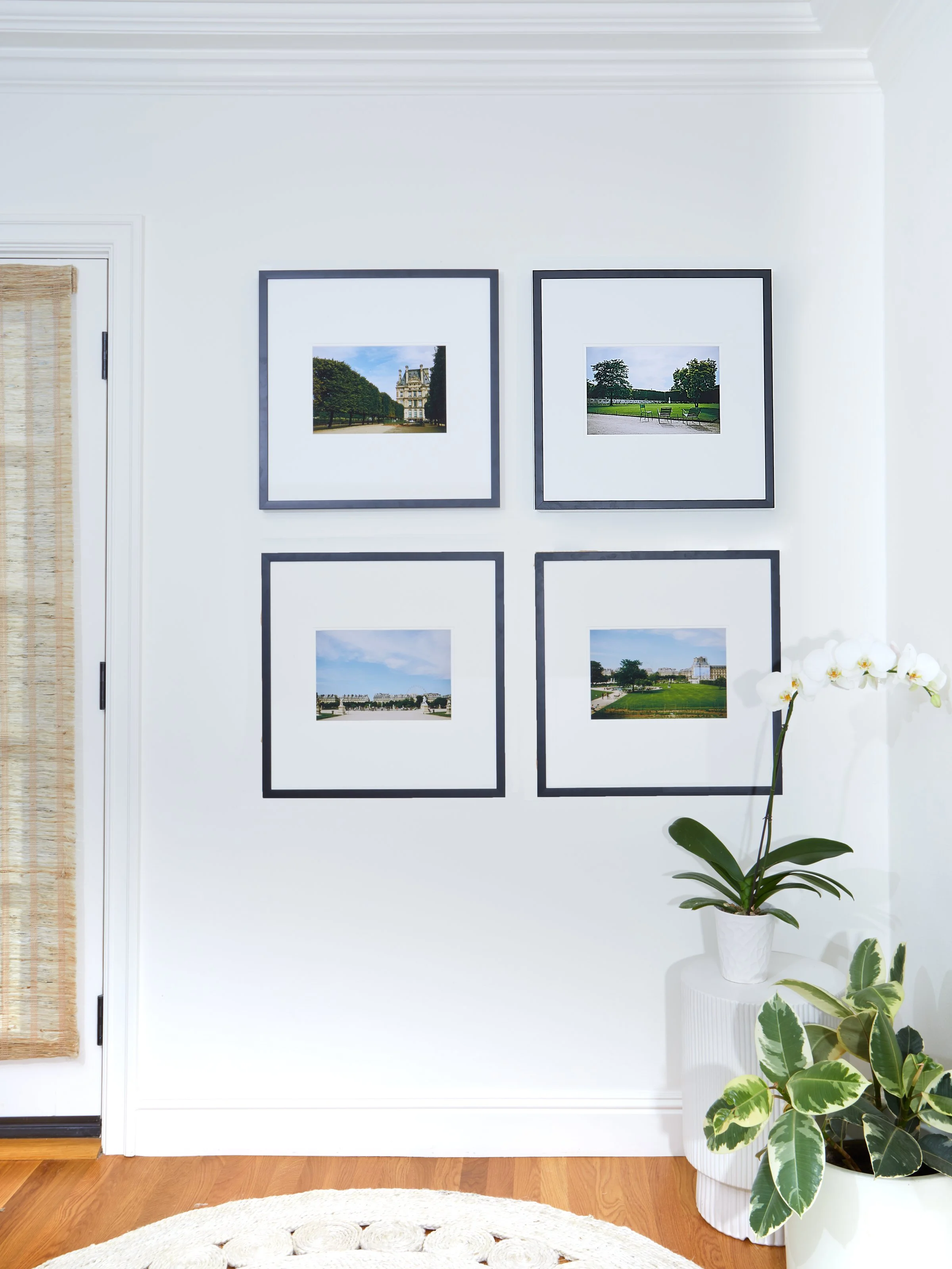 After photo of a finished gallery wall with four matching black frames displaying landscape photography in a two-by-two symmetrical arrangement above a round jute rug