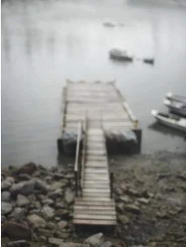 A wooden dock extending into a calm body of water with small boats floating nearby.