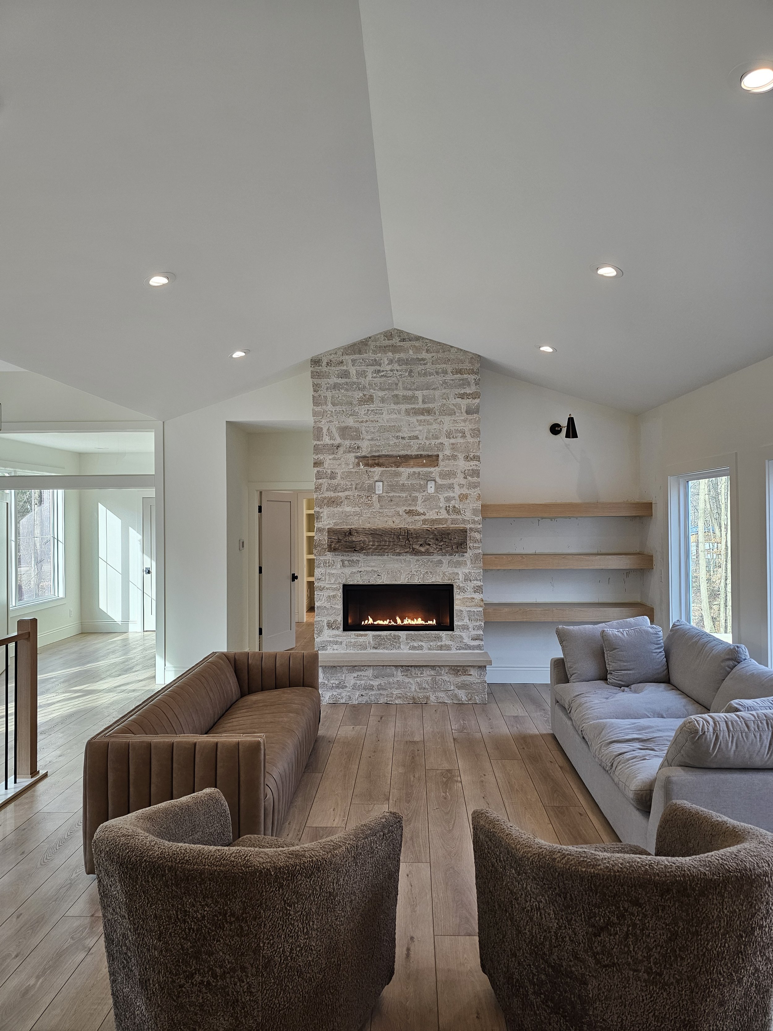 Living room with a brick fireplace, two sofas, two armchairs, wooden floors, and built-in wall shelves. This beautiful custom home was built by Oakland Construction.