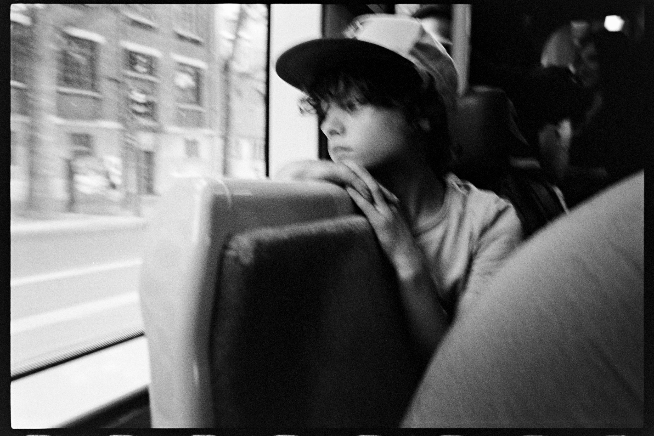 Un adolescents assis dans un bus, regardant par la fenêtre, en noir et blanc.