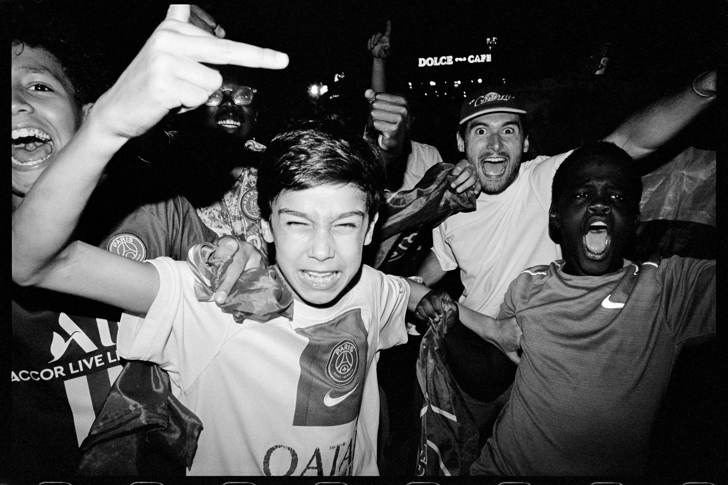 Groupe de personnes expriment leur excitation et joie, certains criant ou levant les bras, lors d'une célébration. La majorité portent des vêtements avec des logos liés au football.