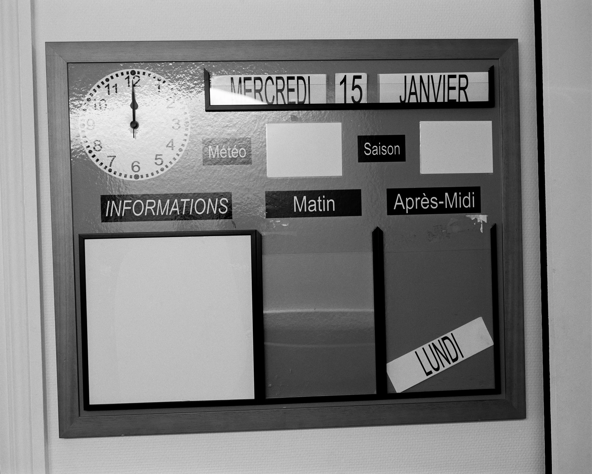 Un tableau d'informations avec une horloge, la date, la météo, et des sections pour le matin et l'après-midi, avec un espace pour l'information et un autre pour le jour de la semaine, qui indique "Lundi".