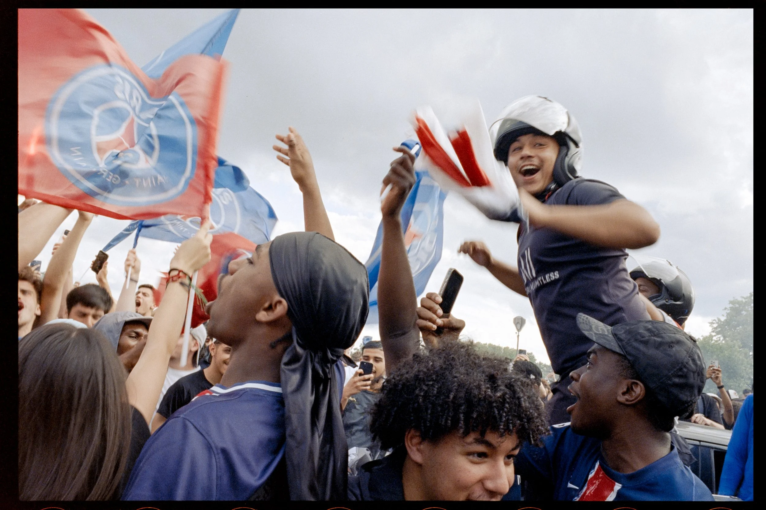 Jeunes supporters en fête, portant des drapeaux, certains avec des casques, manifestant leur enthousiasme lors d'une célébration en plein air.